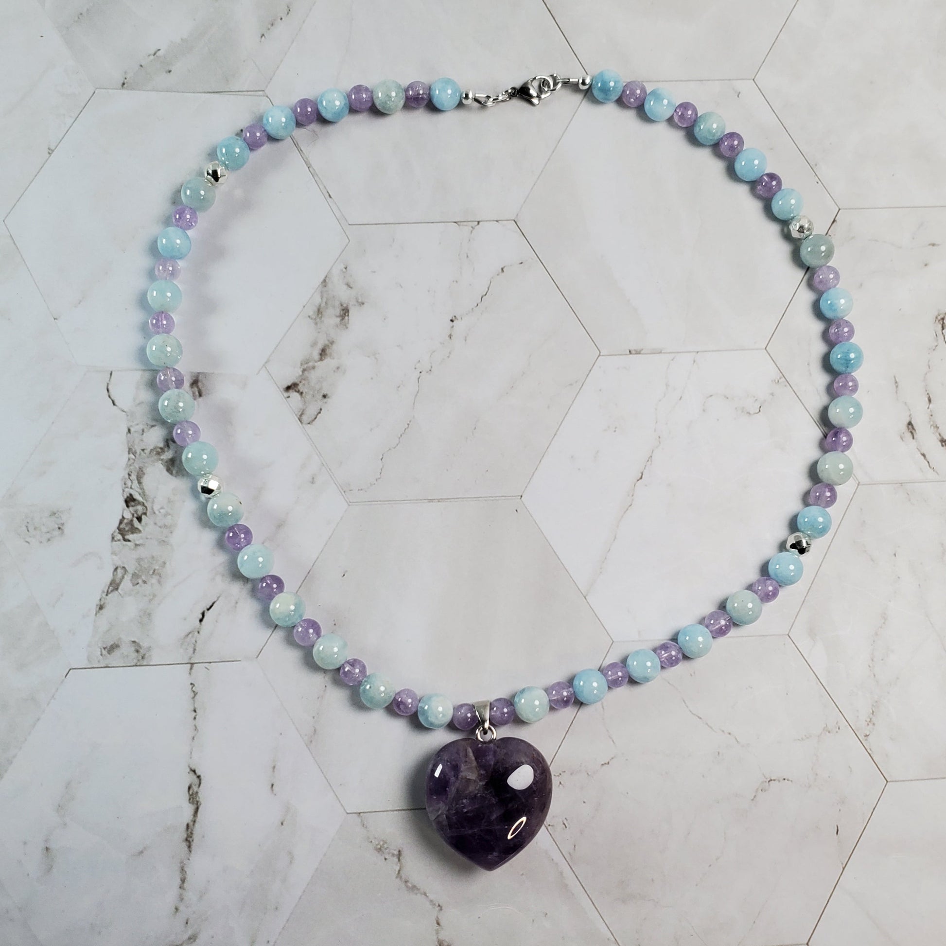 Necklace with multicolored beads and an amethyst pendant on a marble surface