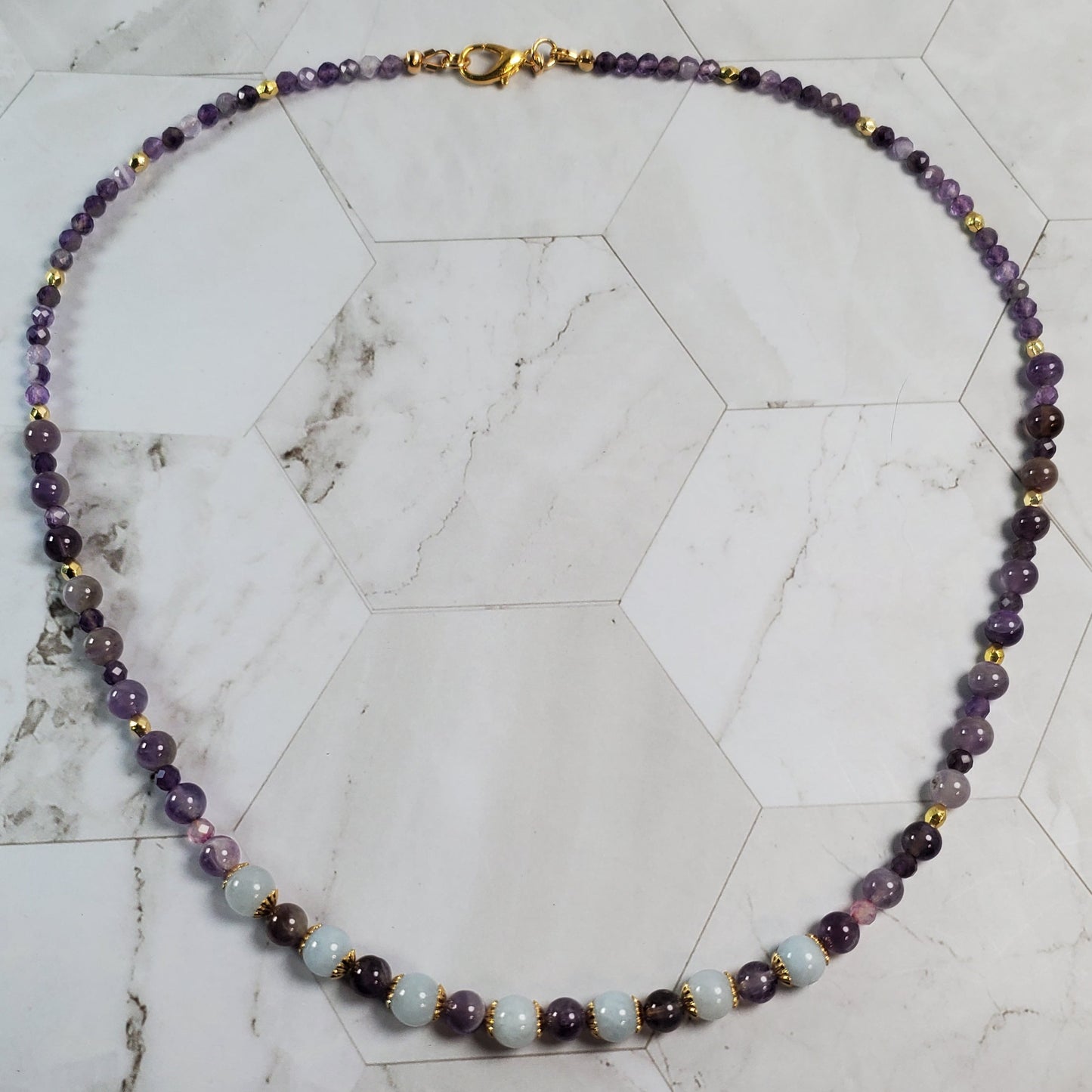 Necklace with purple and gold beads on a marble surface