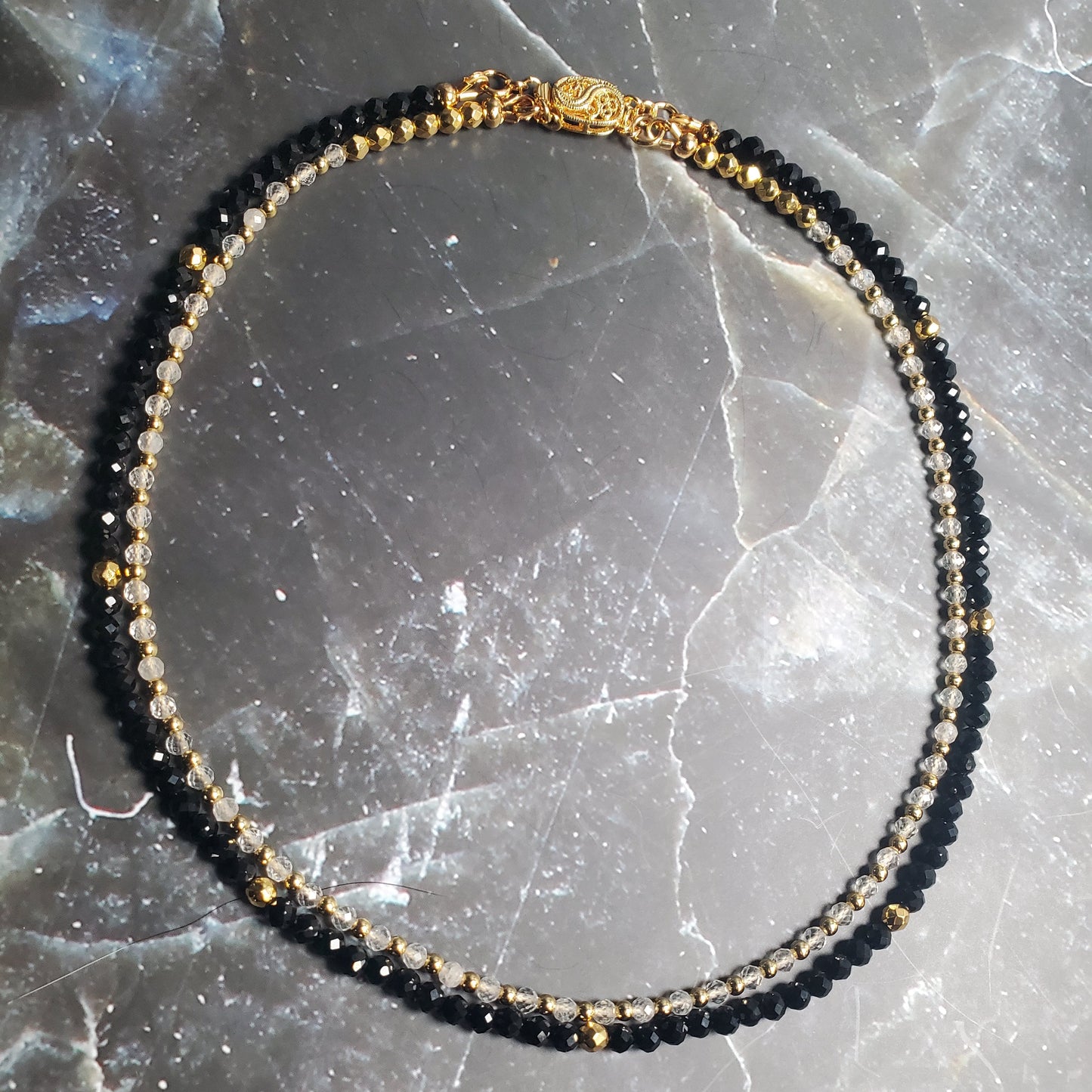 Black and gold beaded necklace on a textured gray surface