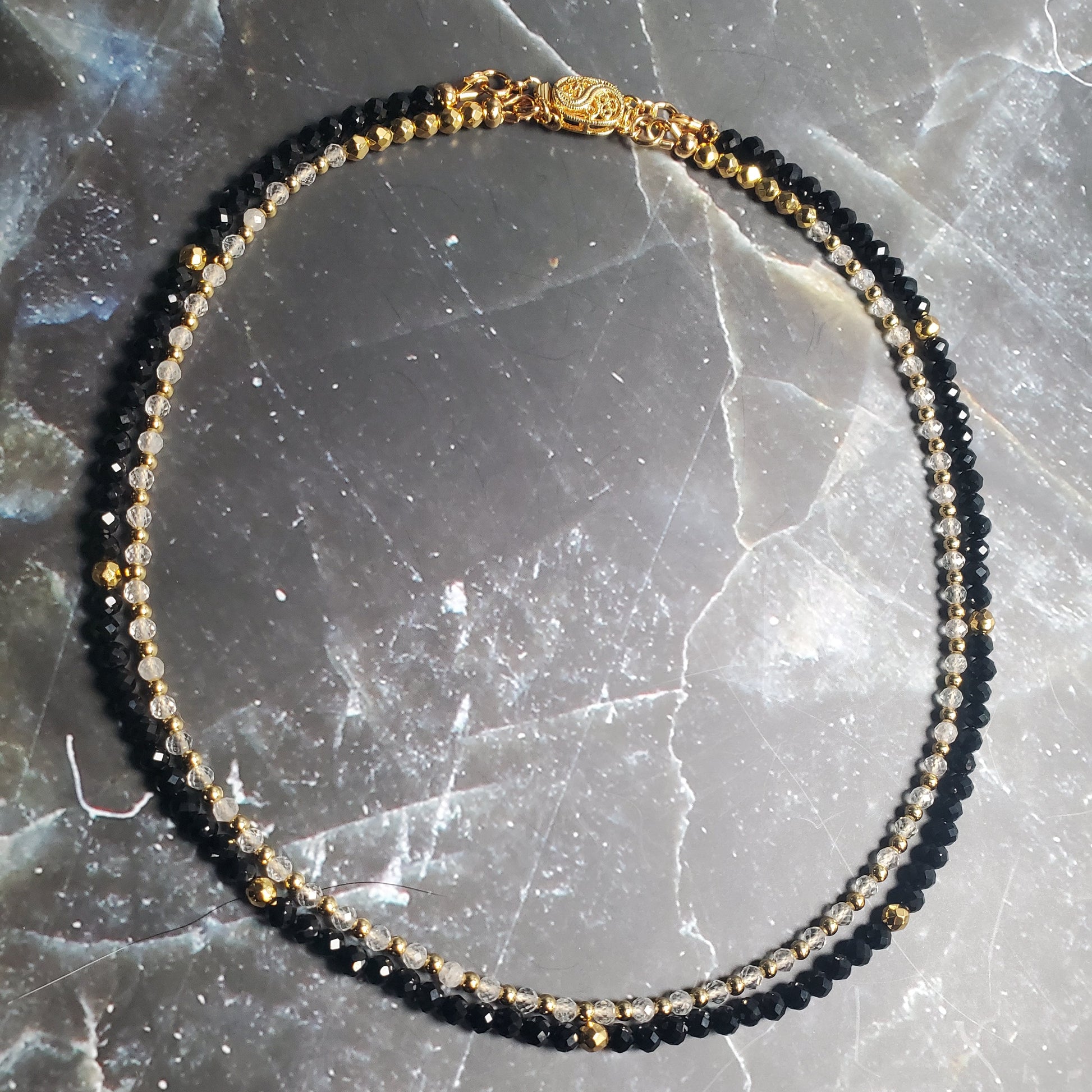 Black and gold beaded necklace on a textured gray surface