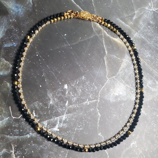 Black and gold beaded necklace on a textured gray surface