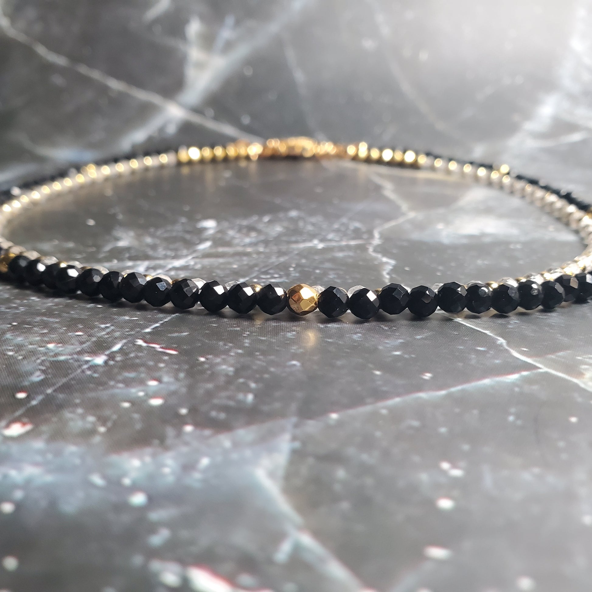Black beaded Necklace with gold accents on a gray marble surface