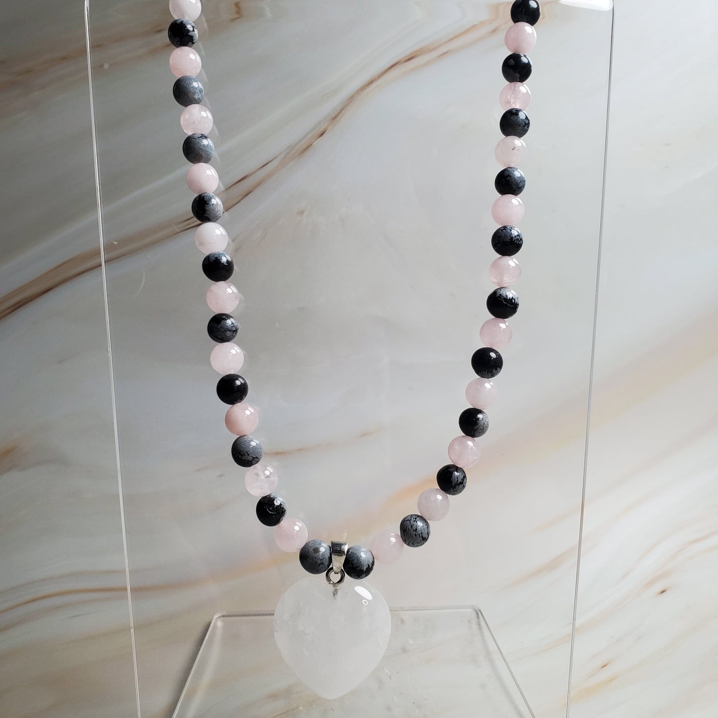 Black, white, and pink beaded necklace on a clear stand against a marble background