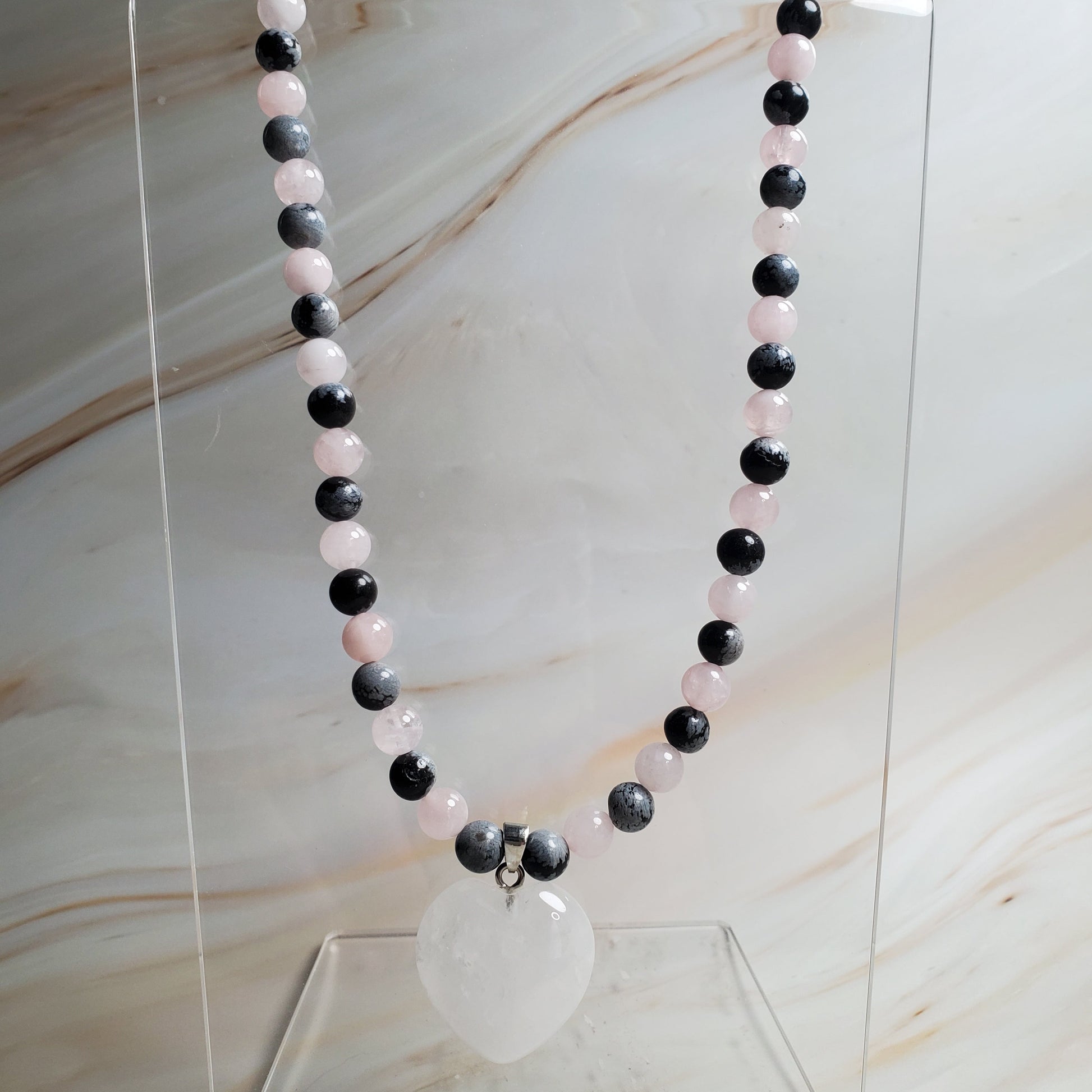 Black, white, and pink beaded necklace on a clear stand against a marble background