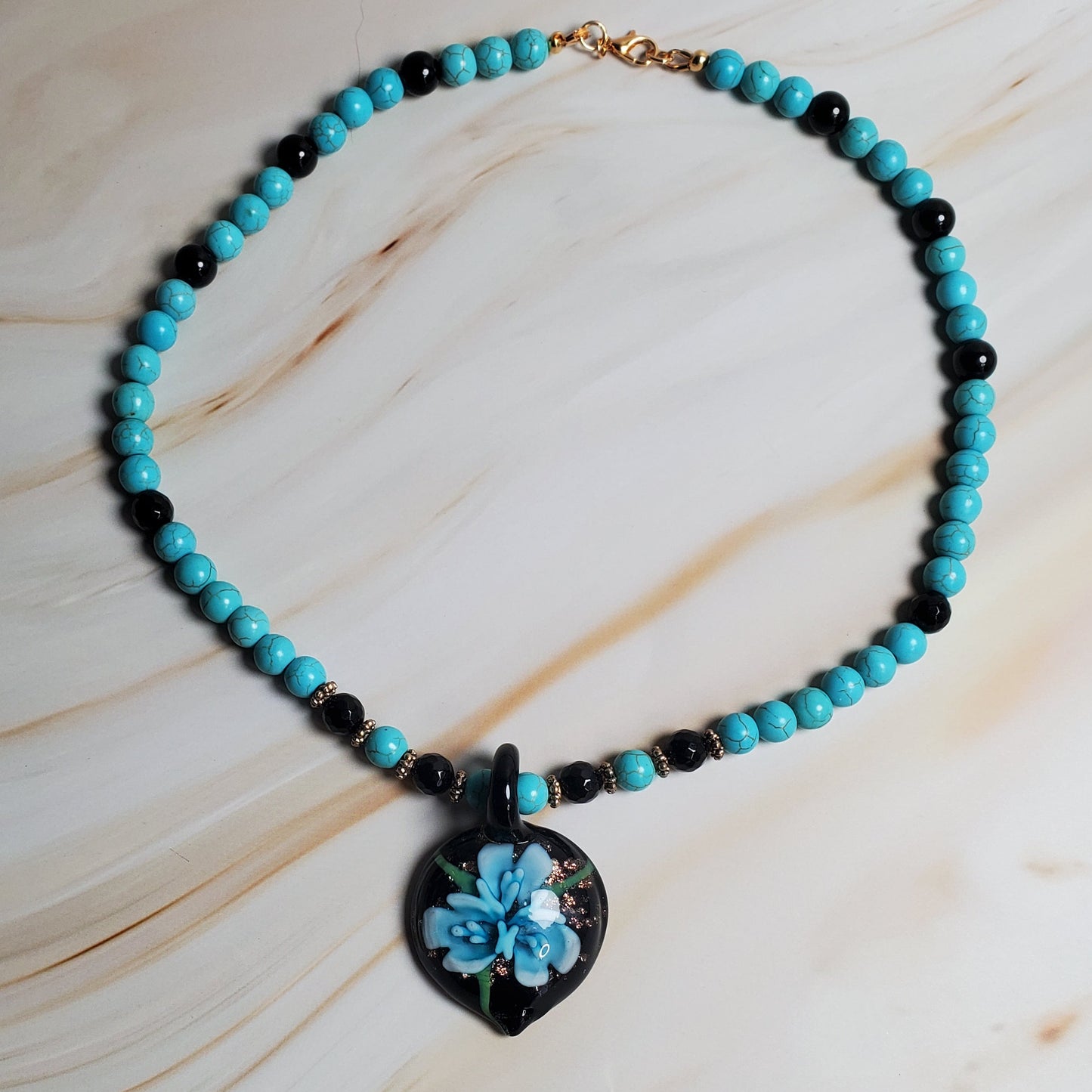 Necklace with turquoise beads and a floral pendant on a marble surface