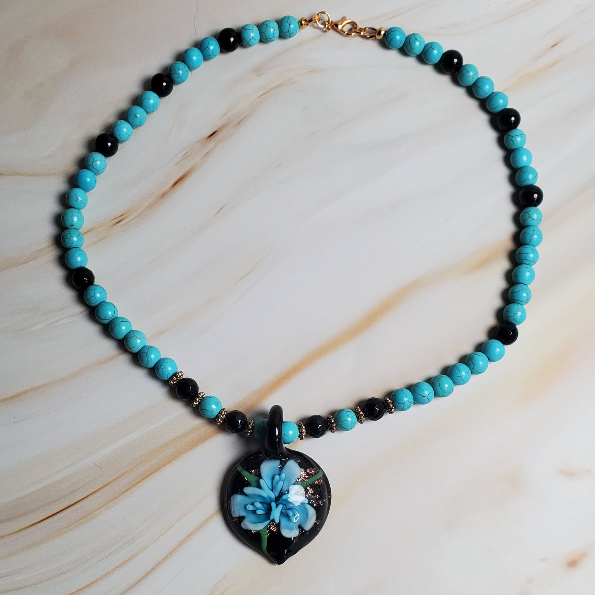 Necklace with turquoise beads and a floral pendant on a marble surface