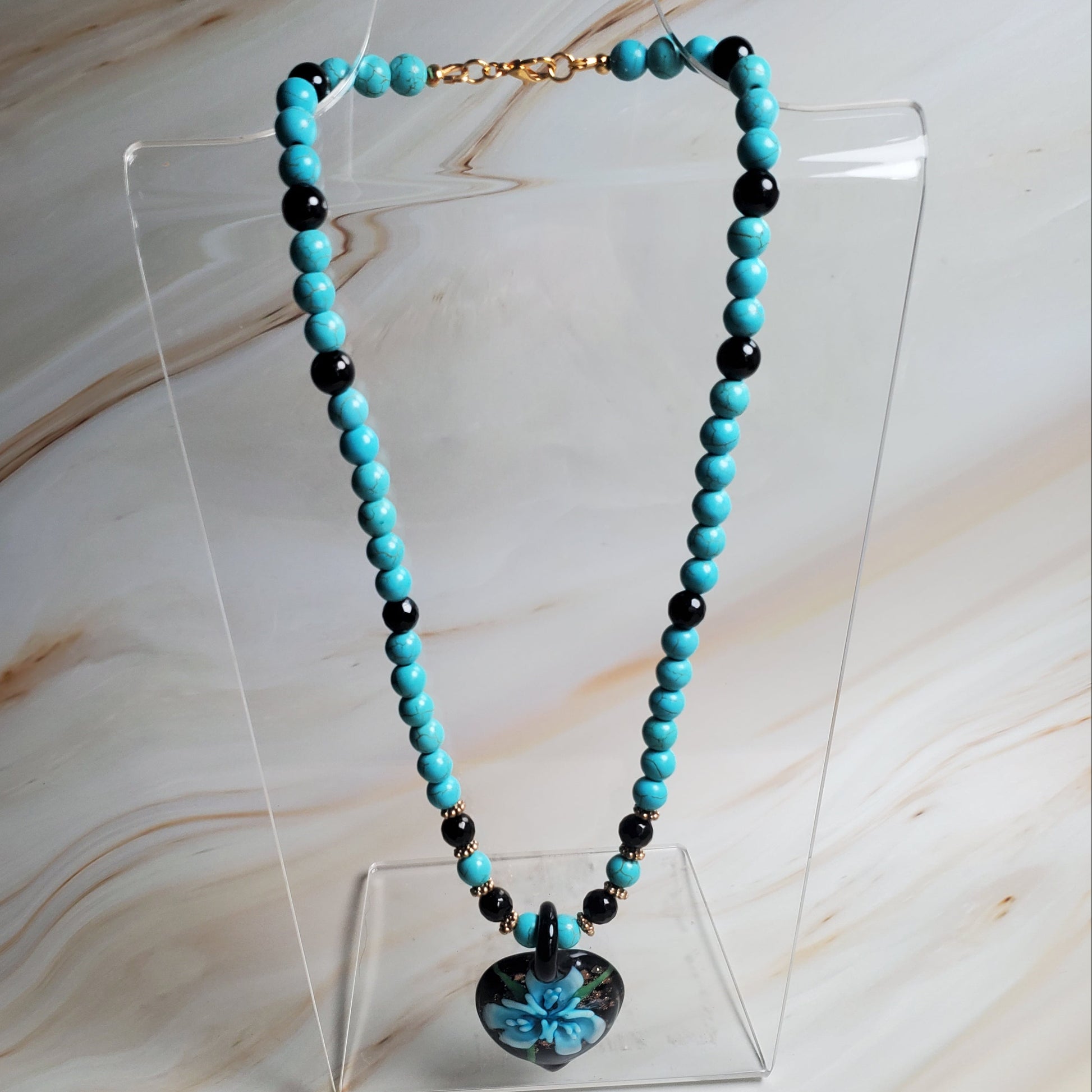 Turquoise and black beaded necklace on a clear stand against a marble background