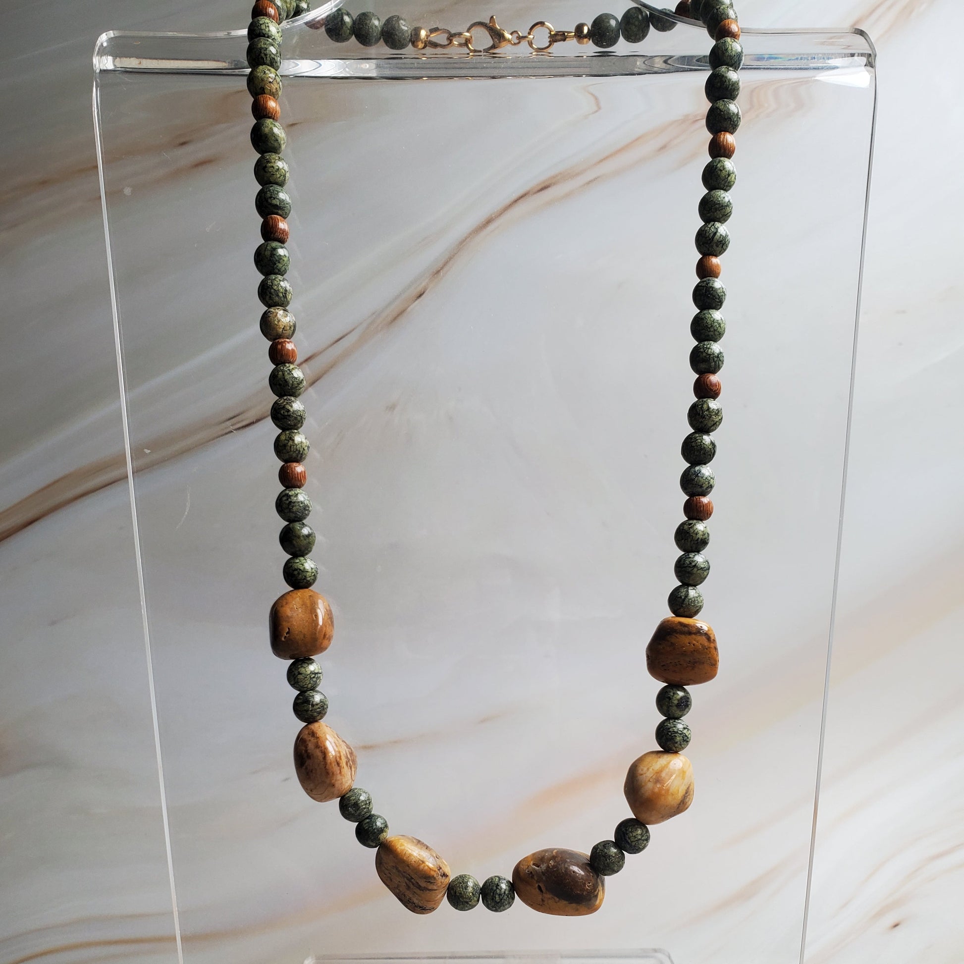 Necklace with wooden beads on a clear stand against a marble background
