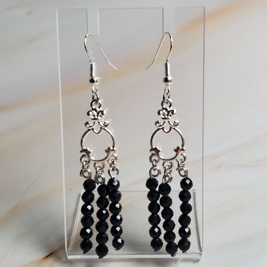 Black beaded earrings on a clear card against a marble background