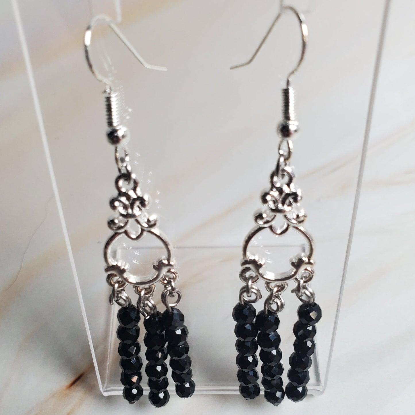 Black beaded earrings on a clear stand against a marble background