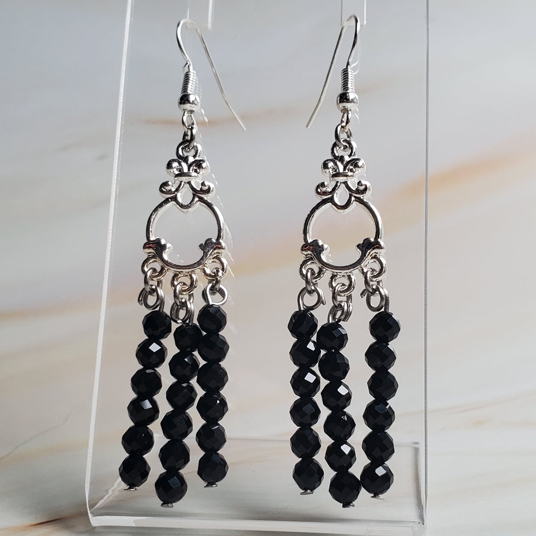 Black beaded earrings on a clear display card against a marble background