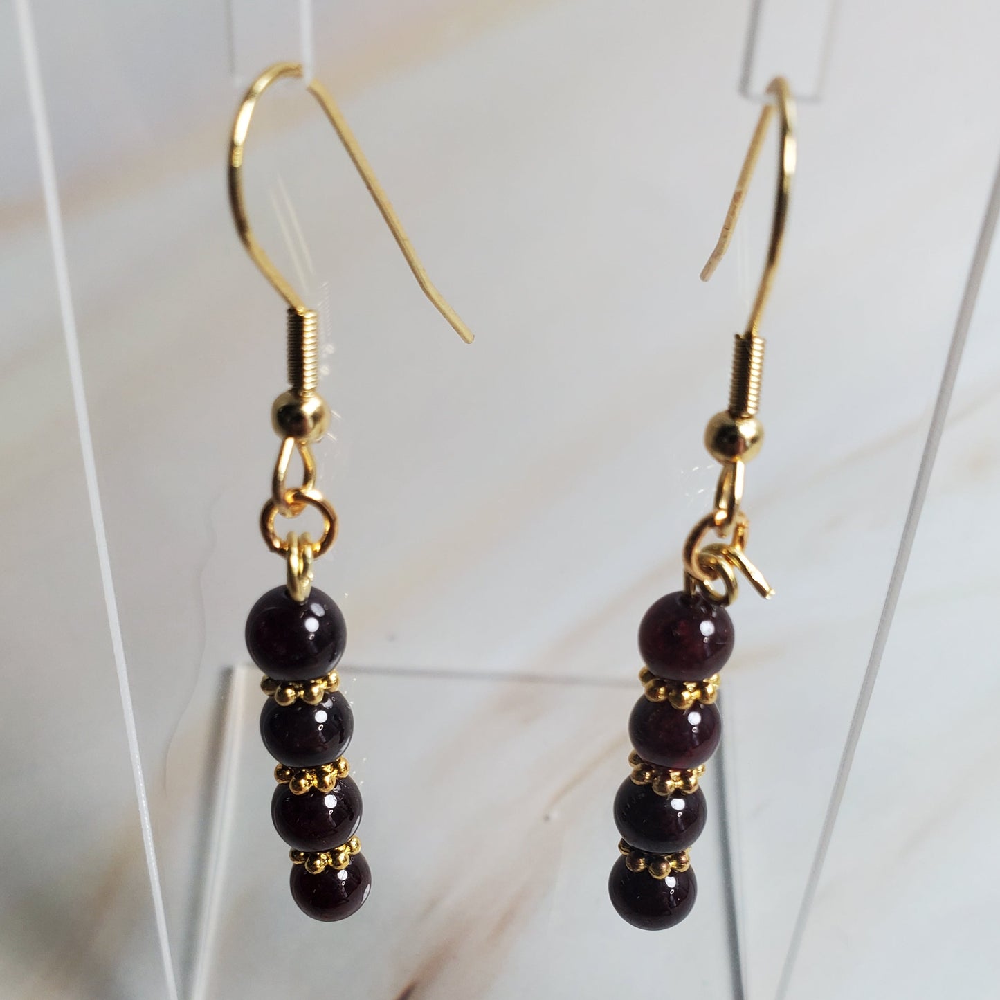 Gold and Garnet beaded earrings on a clear stand against a marble background