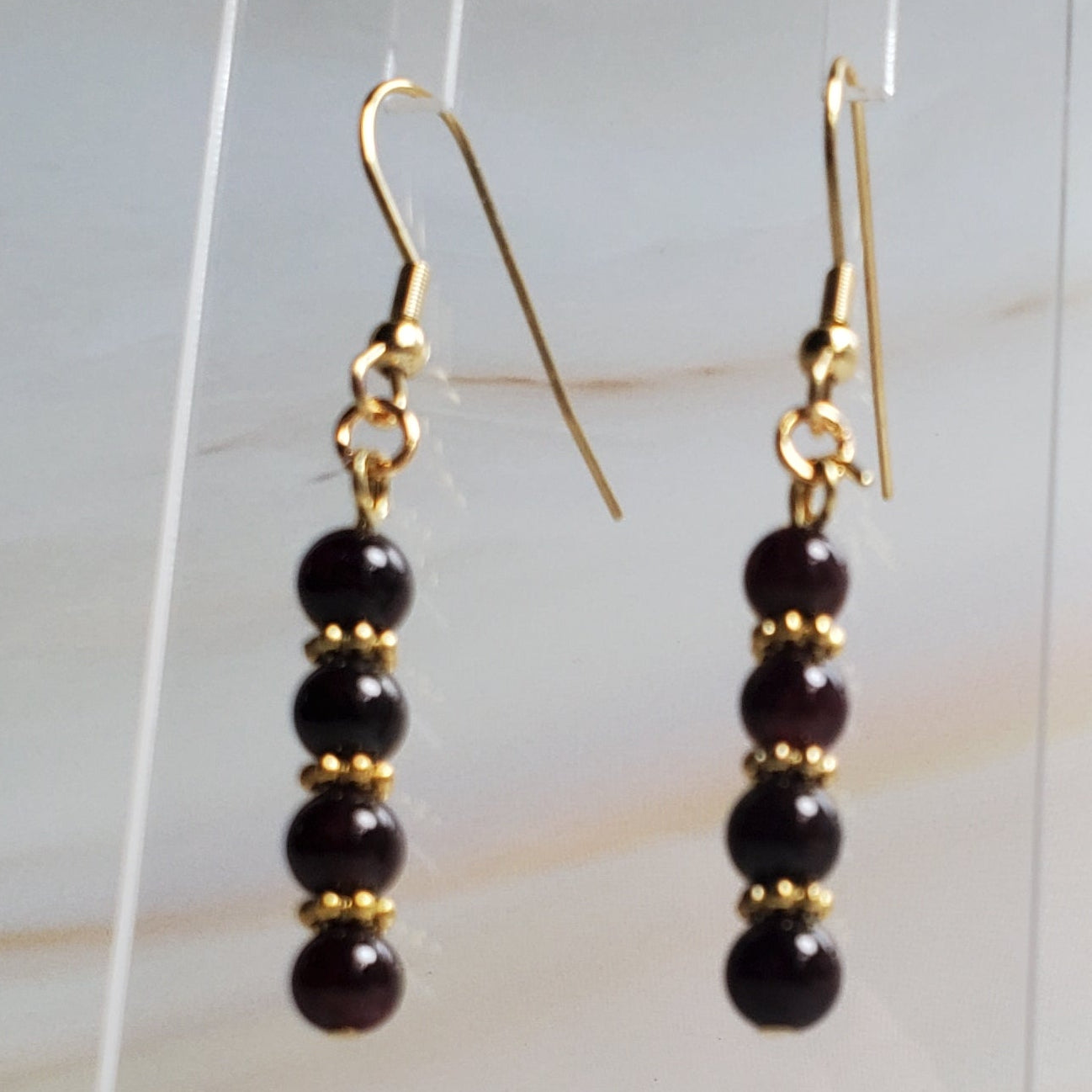 Pair of gold and Garnet beaded earrings on a clear stand against a marble background