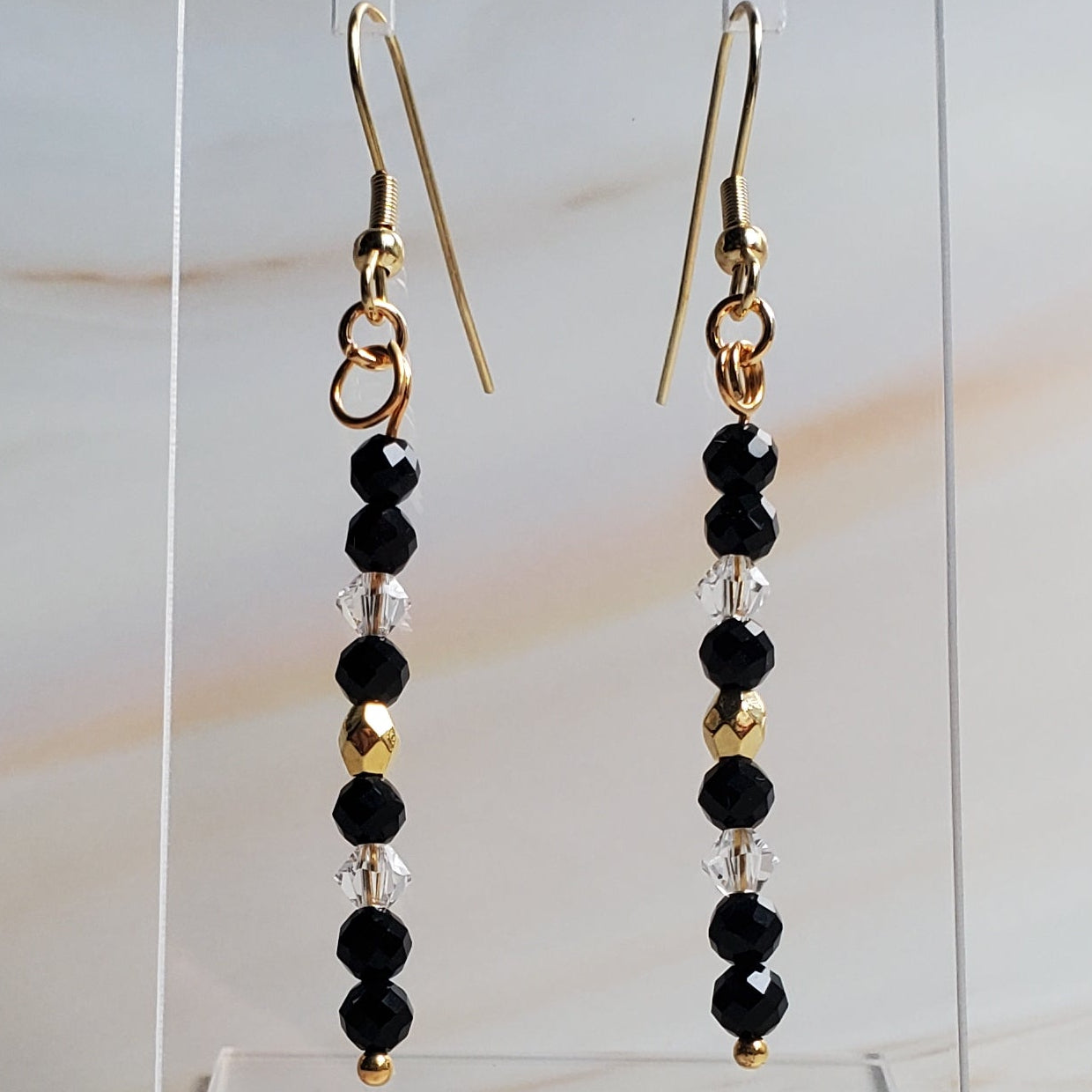 Pair of black beaded earrings on a clear stand against a marble background