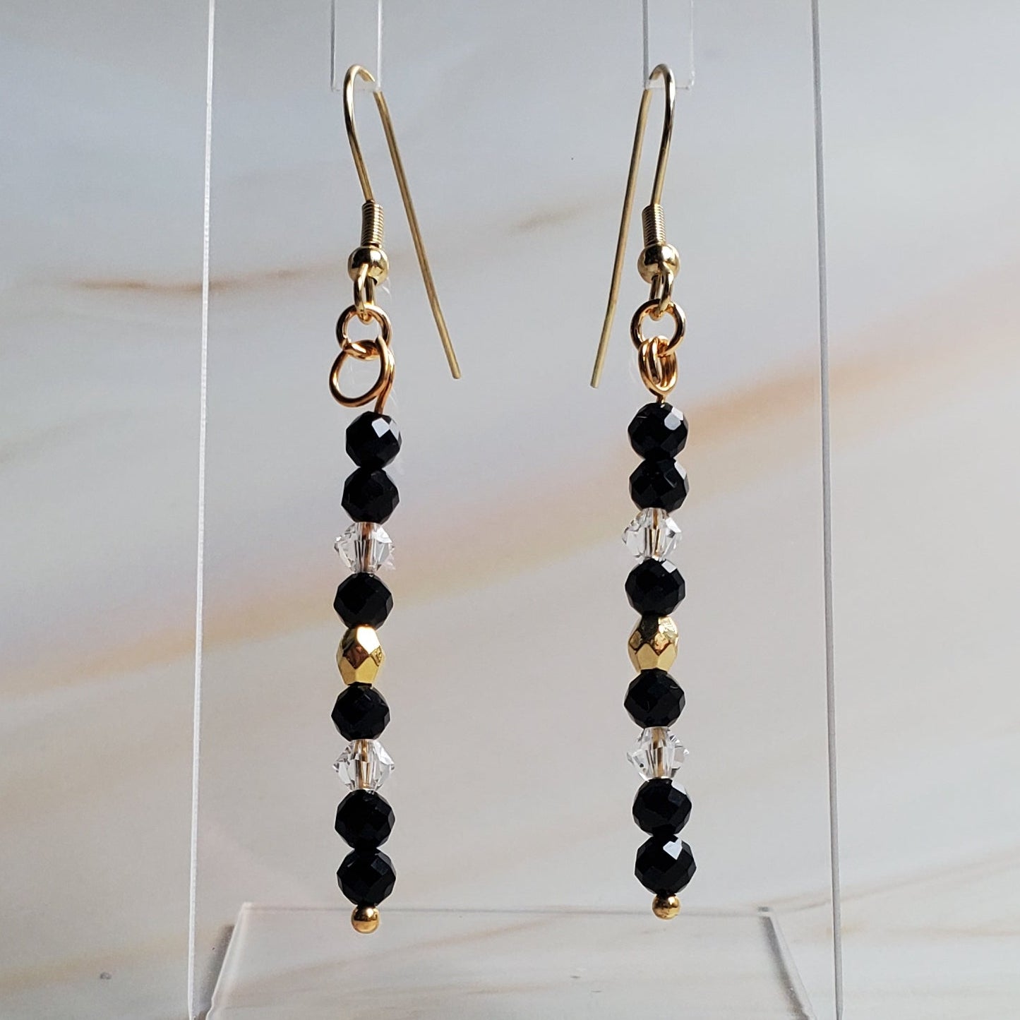 Pair of beaded earrings on a clear stand against a marble background