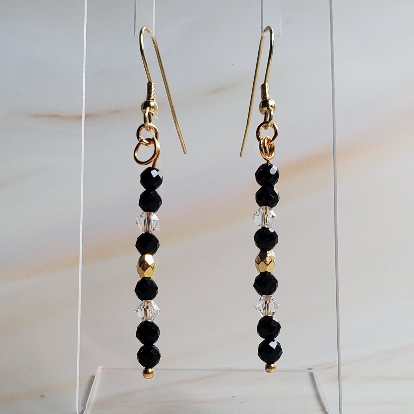 Pair of beaded earrings on a clear stand against a marble background