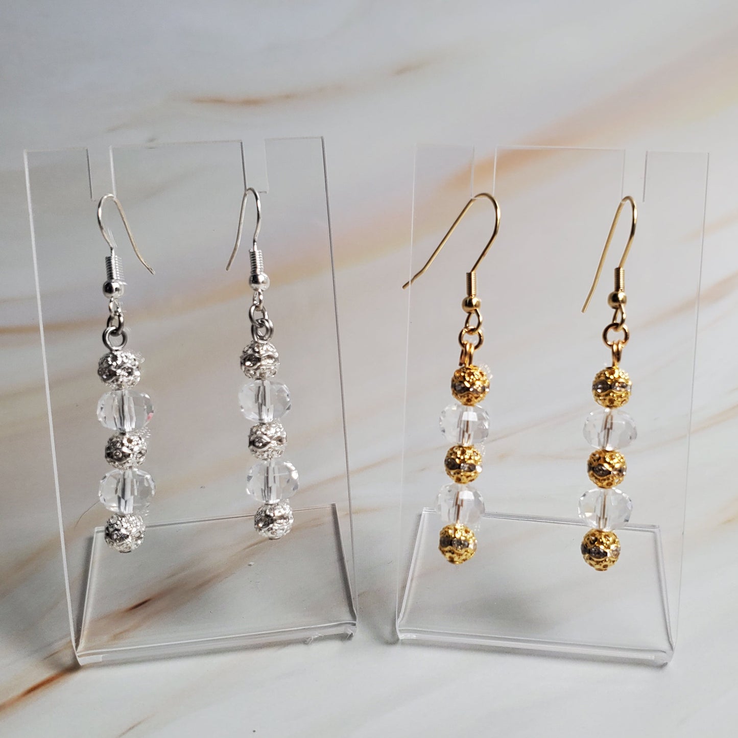 Set of gold and silver beaded earrings on clear stands against a neutral background