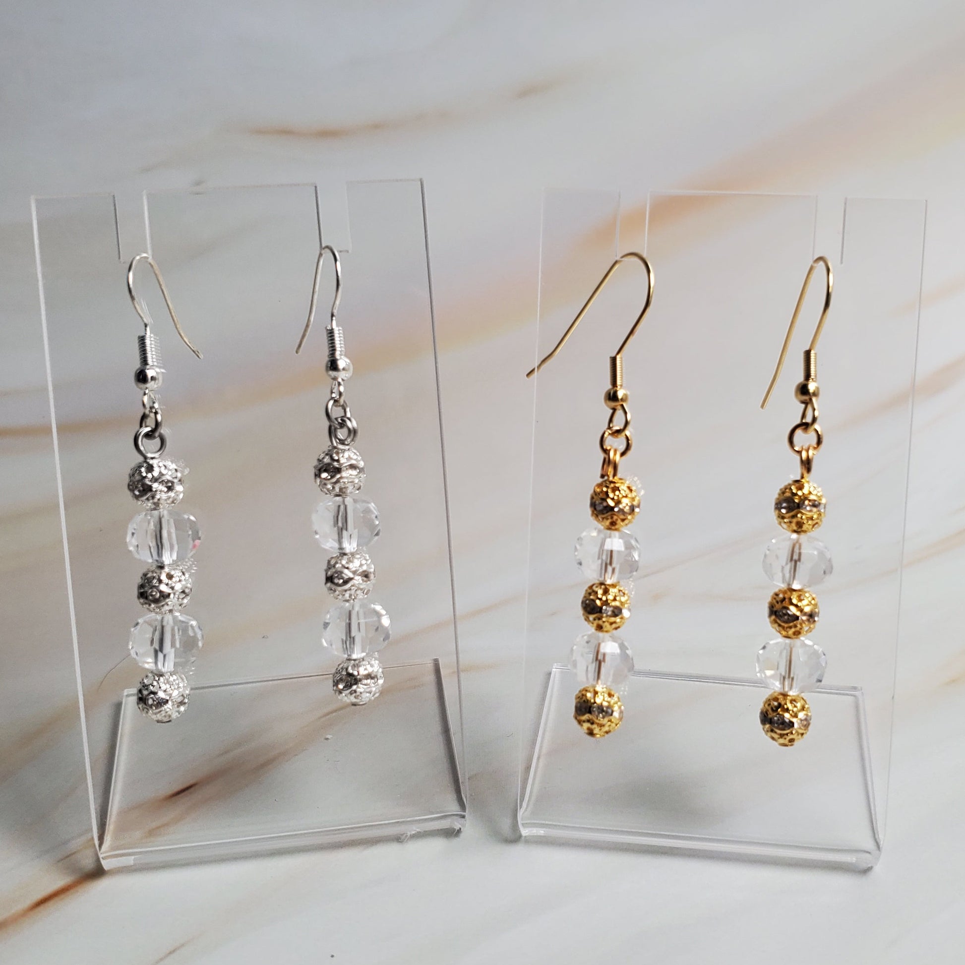 Set of gold and silver beaded earrings on clear stands against a neutral background