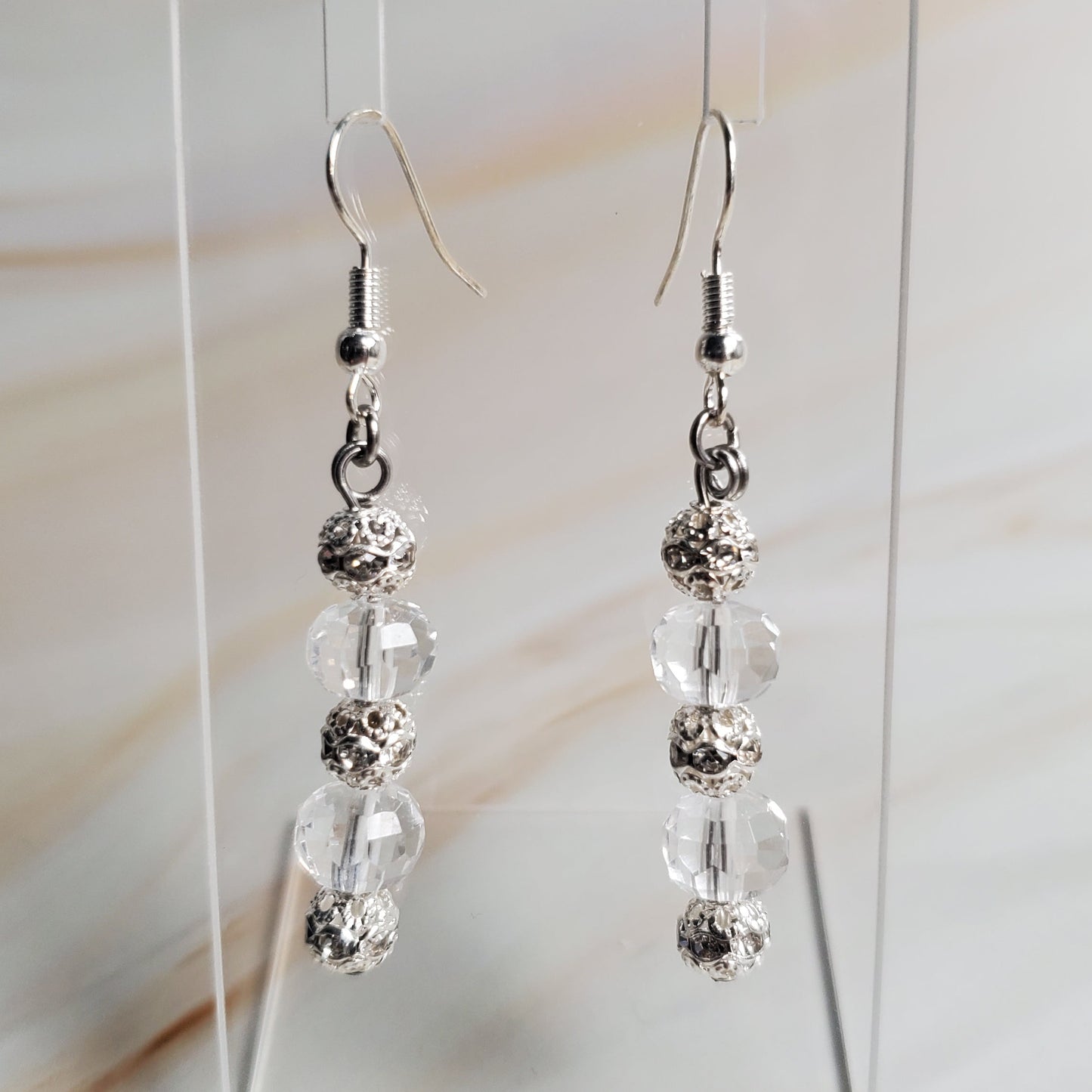 Pair of silver beaded earrings on a clear stand against a neutral background