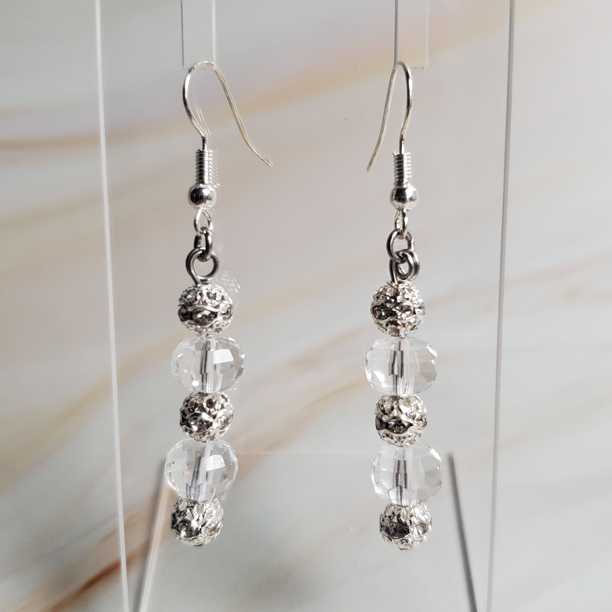 Pair of silver beaded earrings on a clear stand against a neutral background