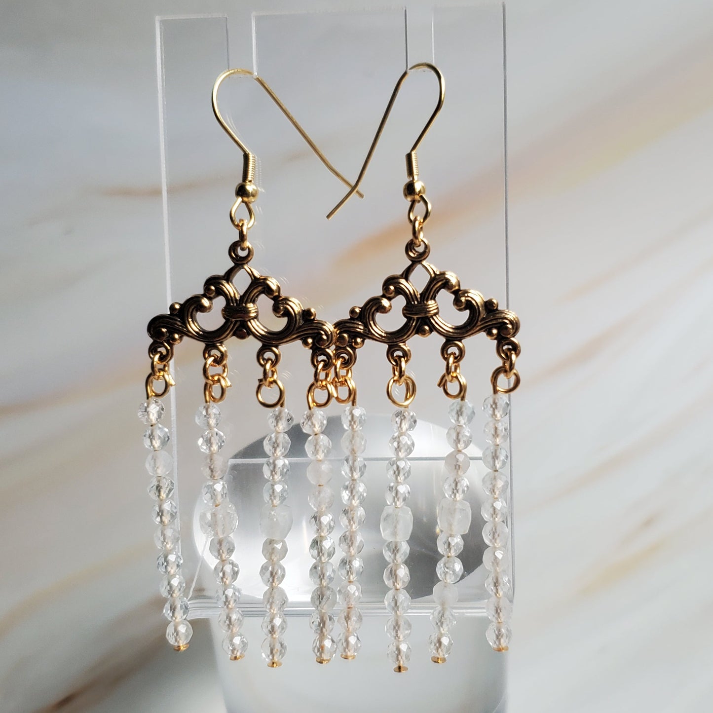 Pair of beaded earrings on a clear stand against a marble background