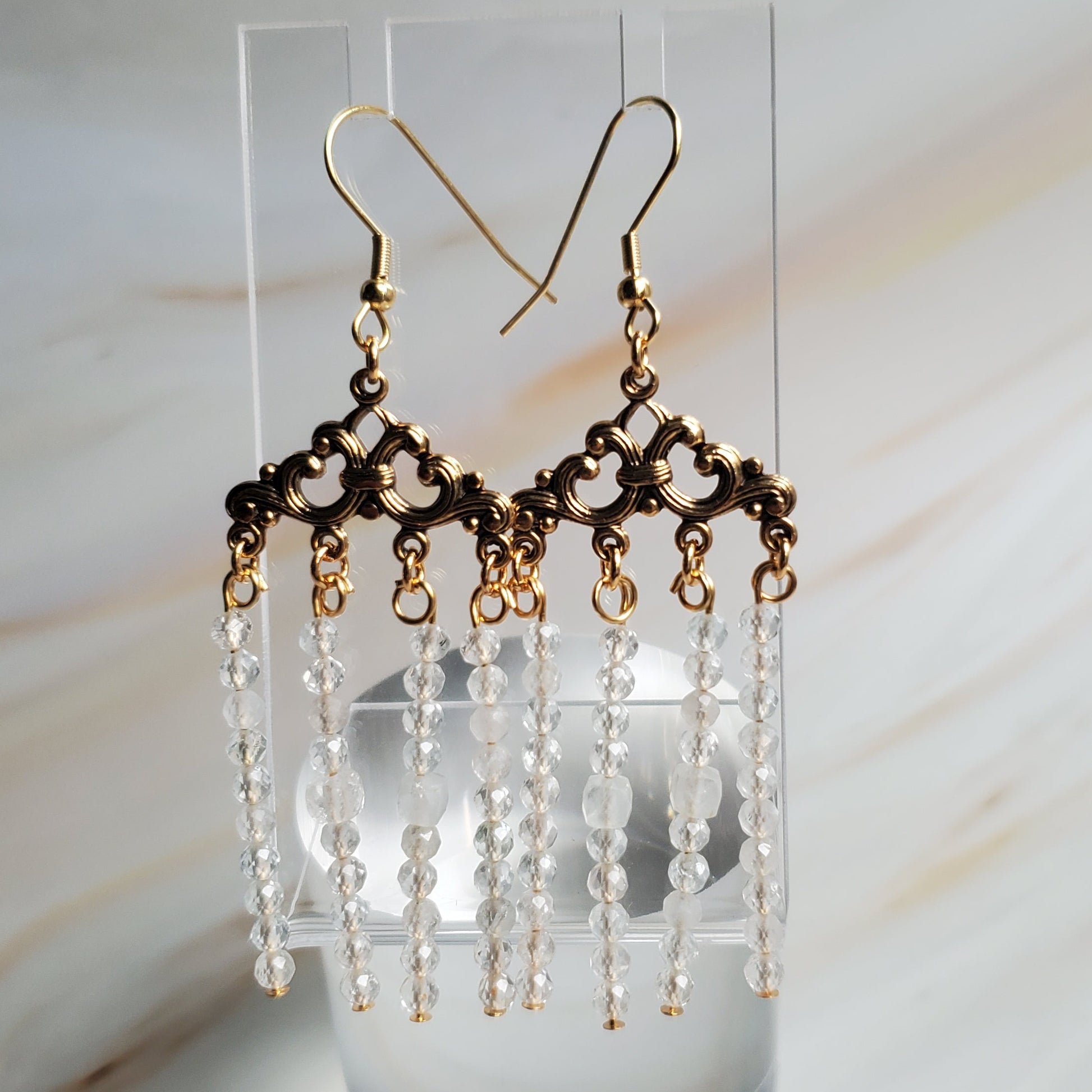 Pair of beaded earrings on a clear stand against a marble background