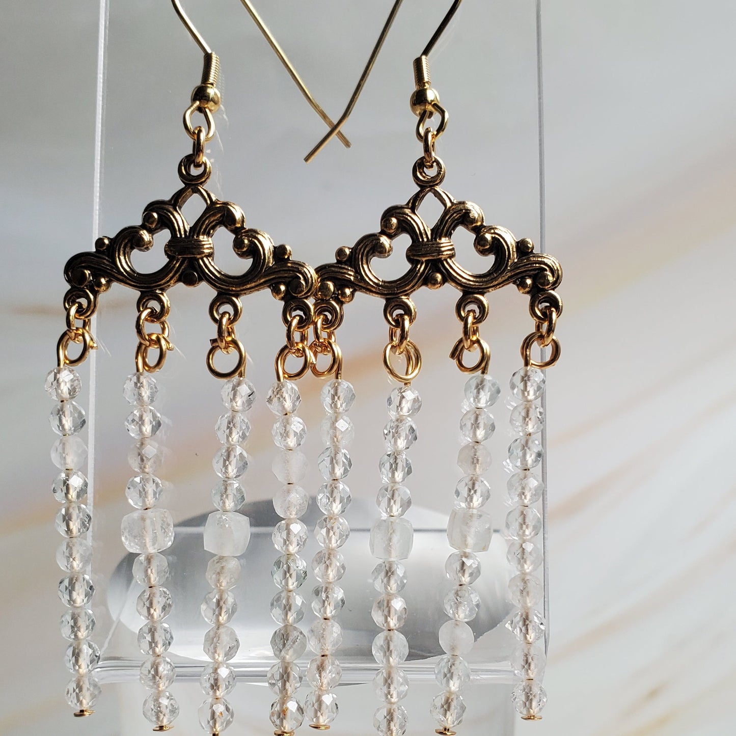 Pair of beaded earrings on a clear stand against a marble background