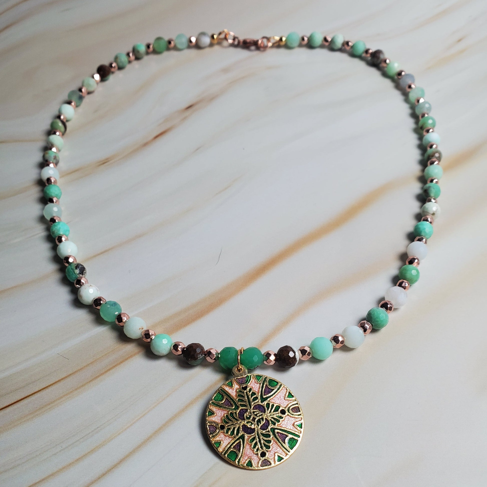 Necklace with green and gold pendant on a light wooden surface