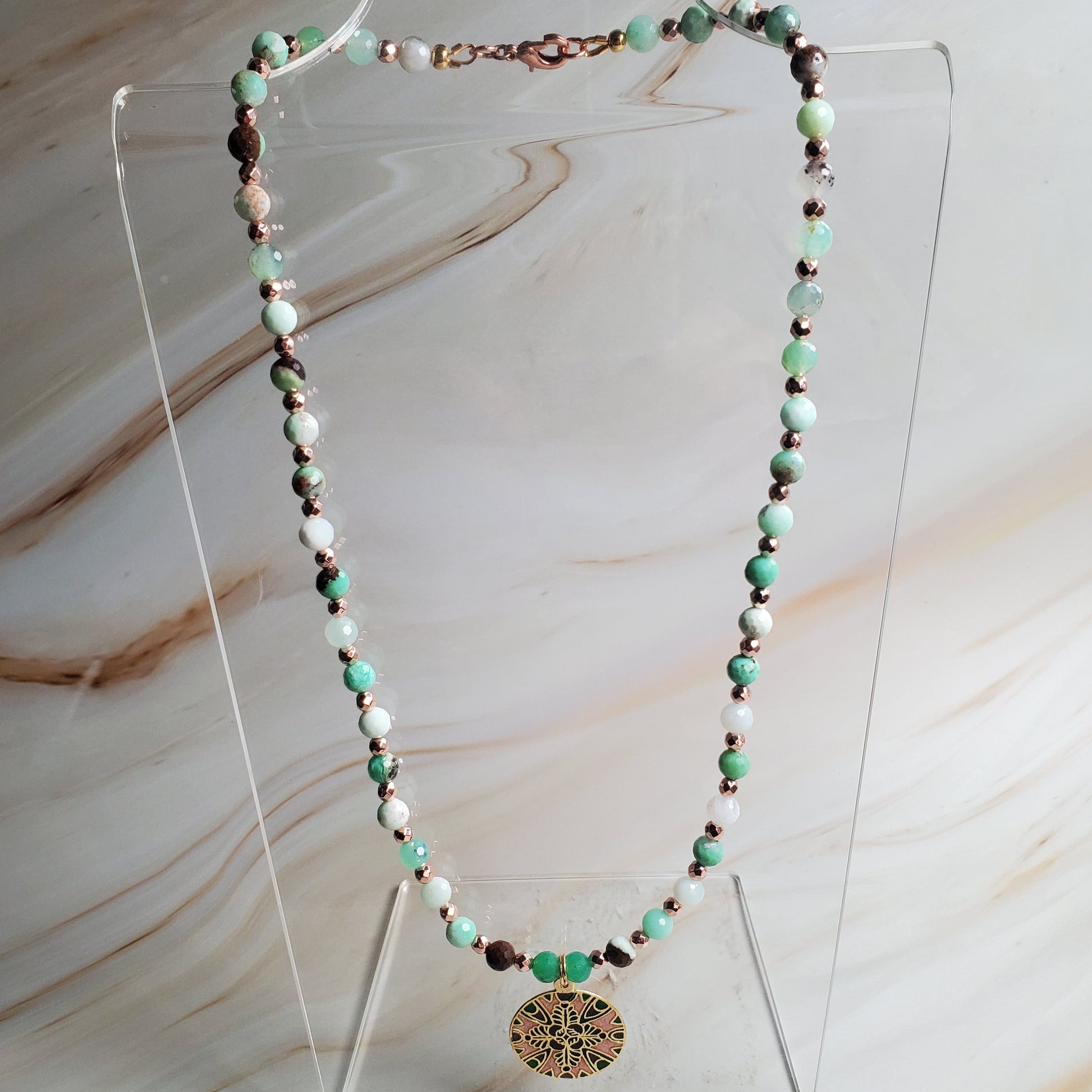 Necklace with green and brown beads on a clear stand against a marble background
