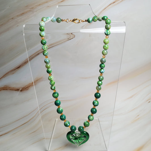 Green beaded necklace on a clear stand against a marble background