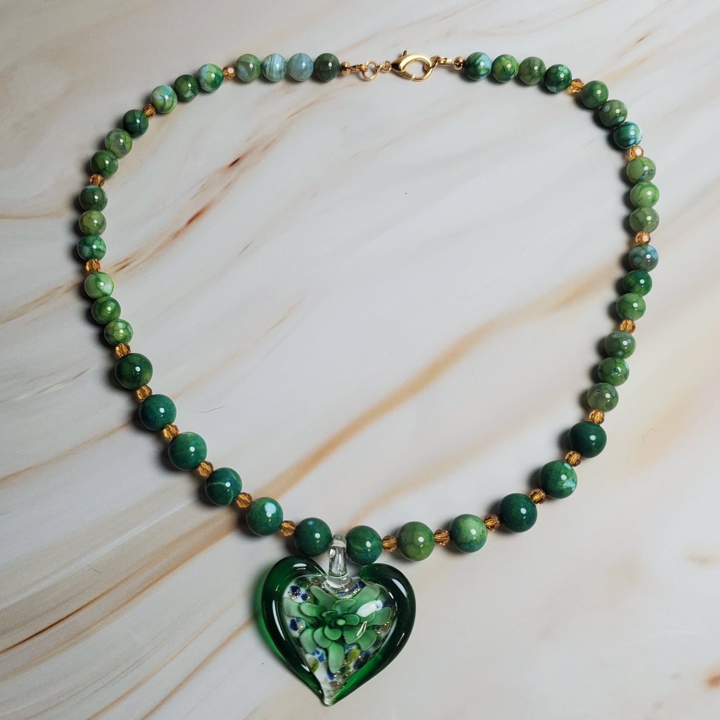 Green beaded necklace with a heart-shaped green pendant on a marble surface