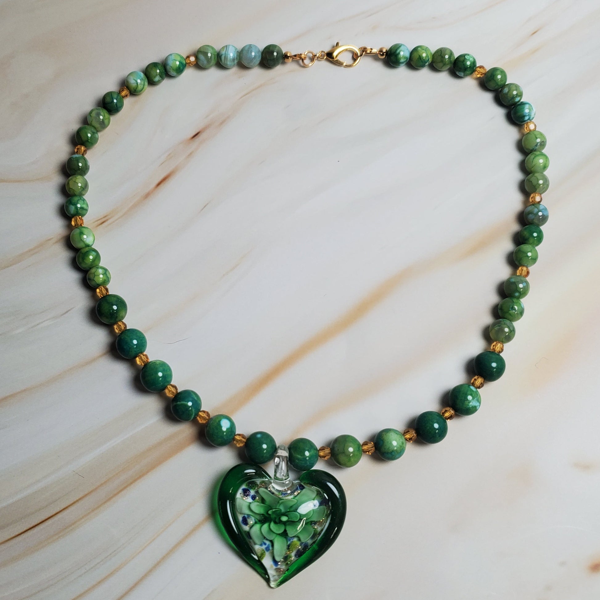 Green beaded necklace with a heart-shaped green pendant on a marble surface