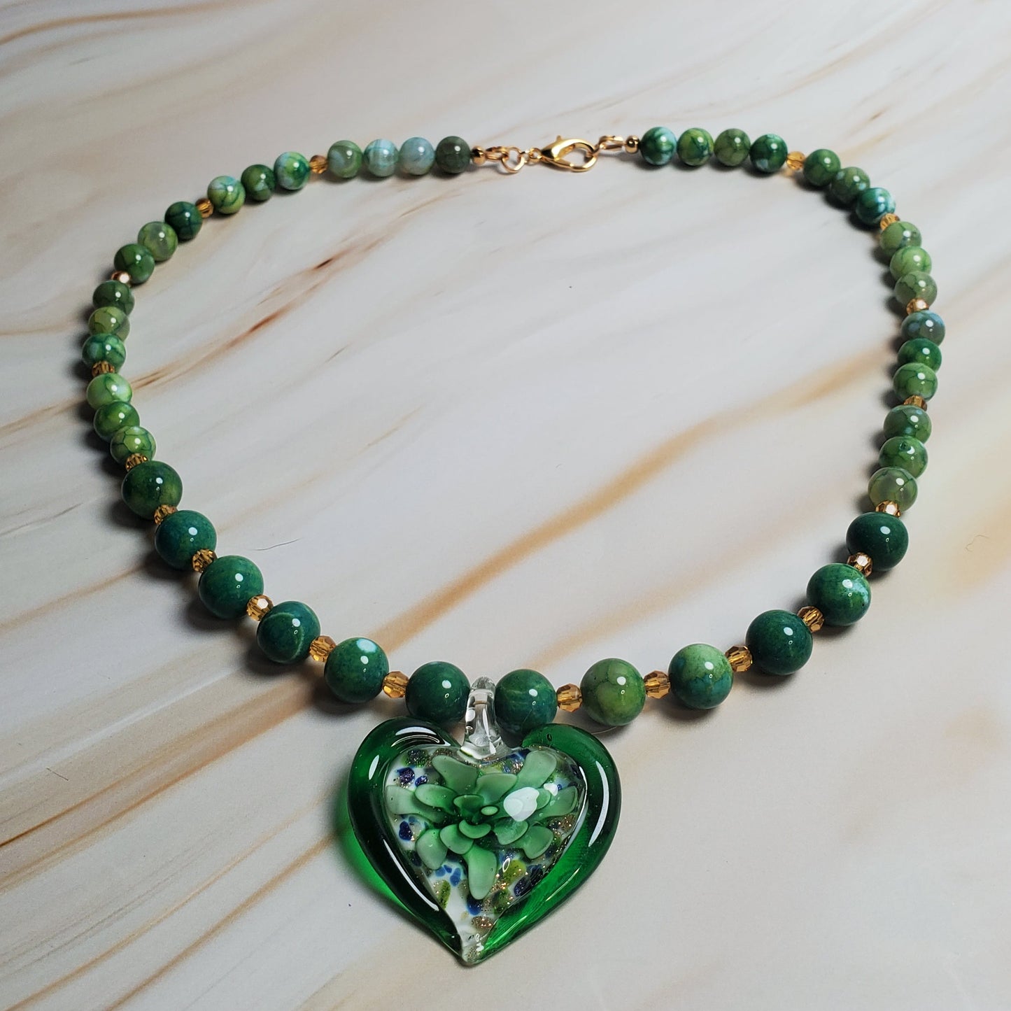 Green beaded necklace with a heart-shaped green pendant on a light marble background
