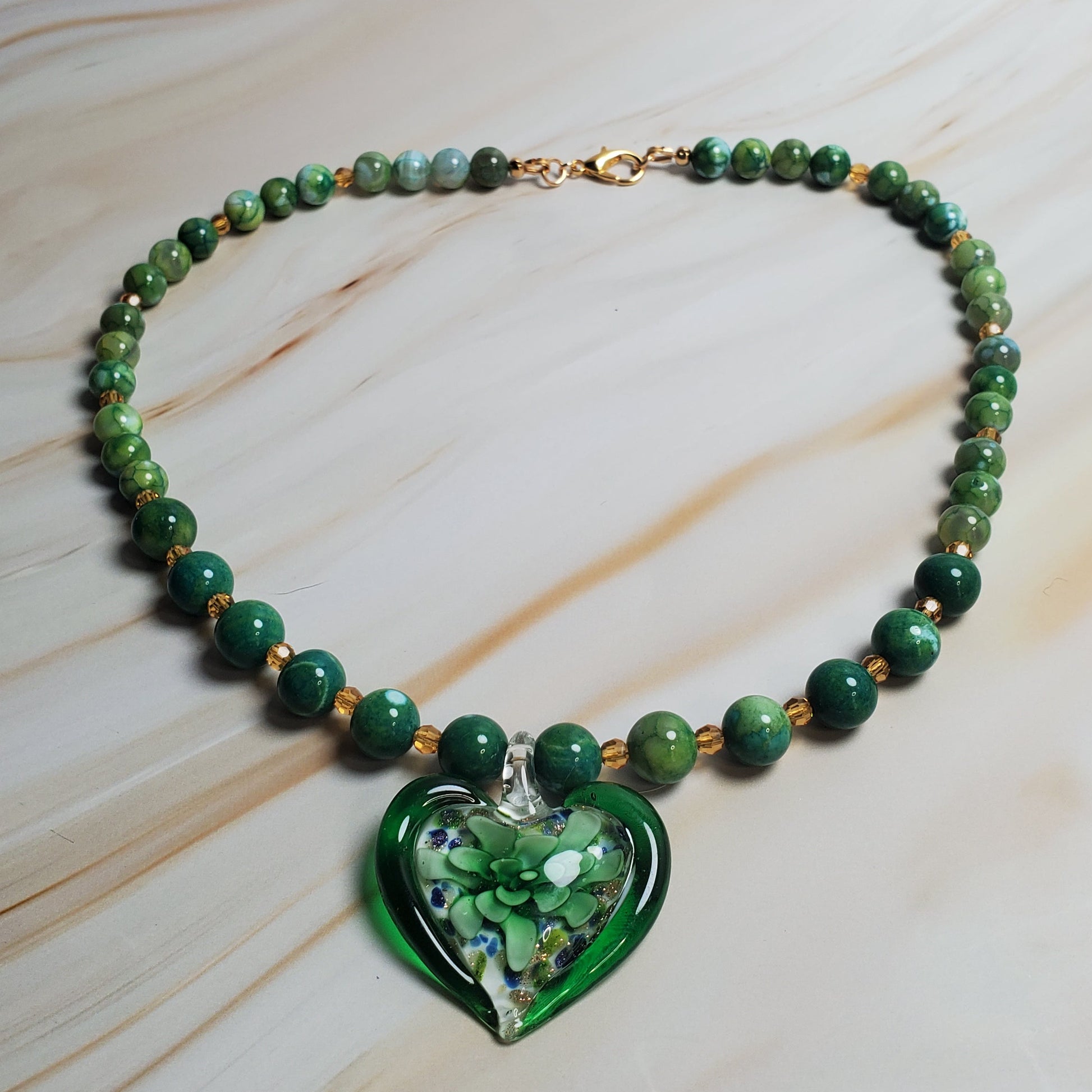 Green beaded necklace with a heart-shaped green pendant on a light marble background
