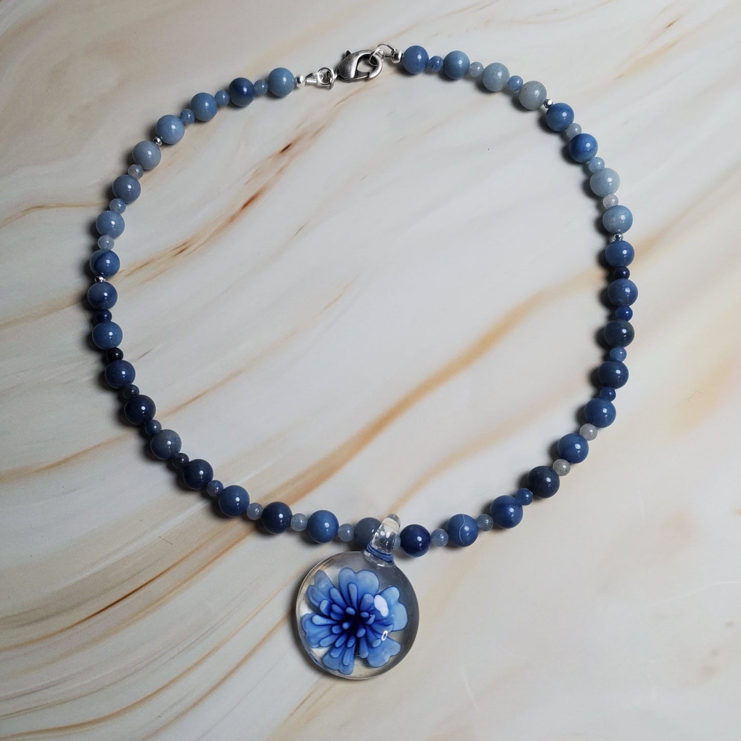 Blue beaded necklace with a floral pendant on a marble surface