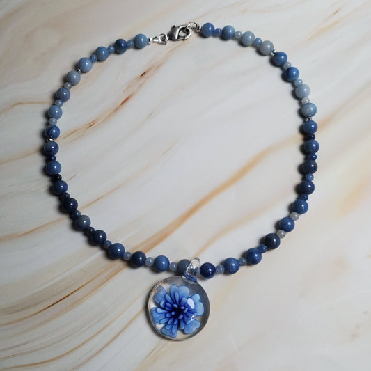 Blue beaded necklace with a floral pendant on a marble surface