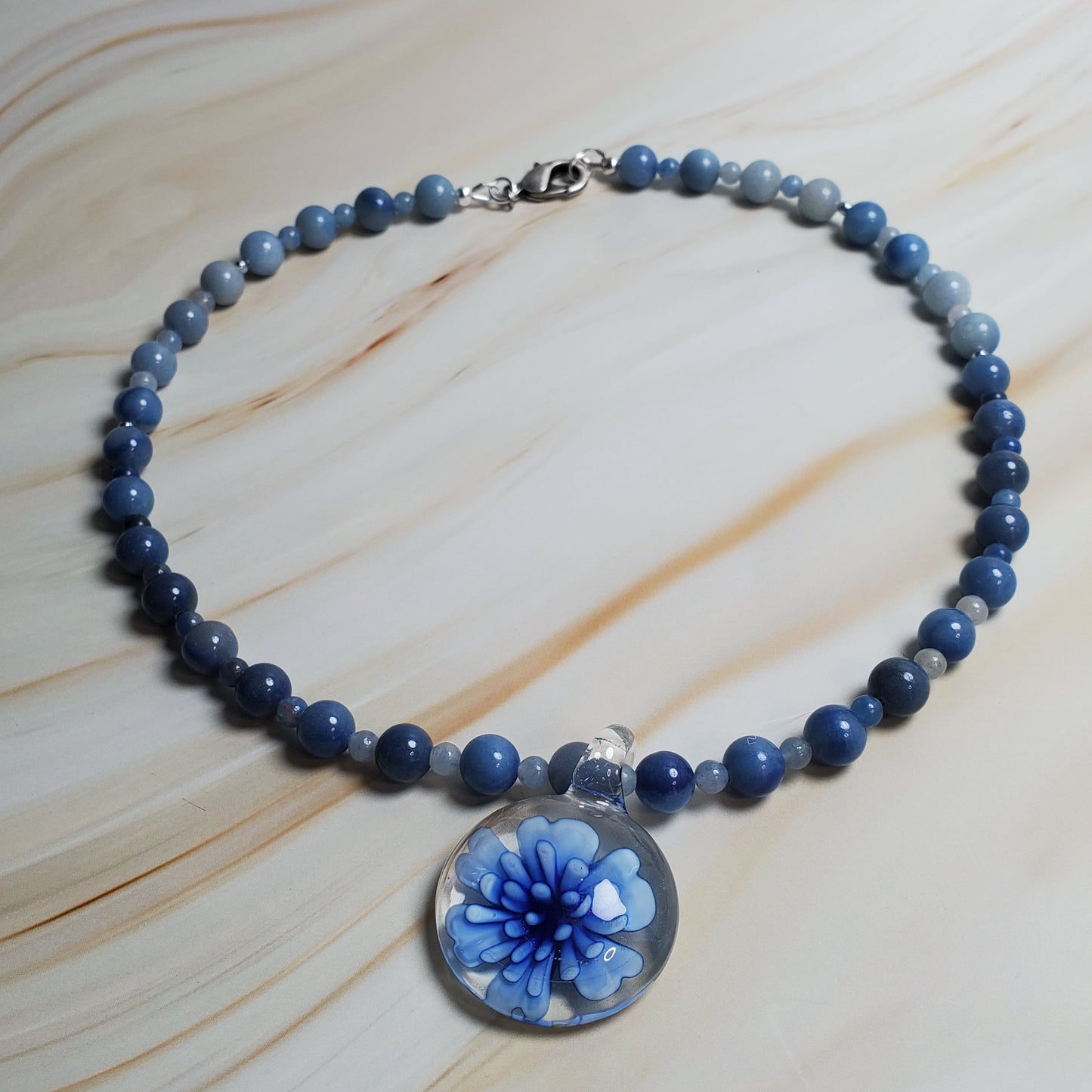 Blue beaded necklace with a floral charm on a light wood surface