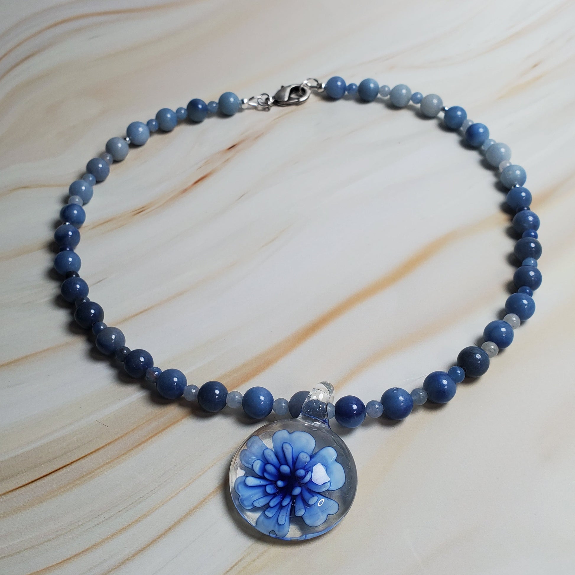 Blue beaded necklace with a floral charm on a light wood surface