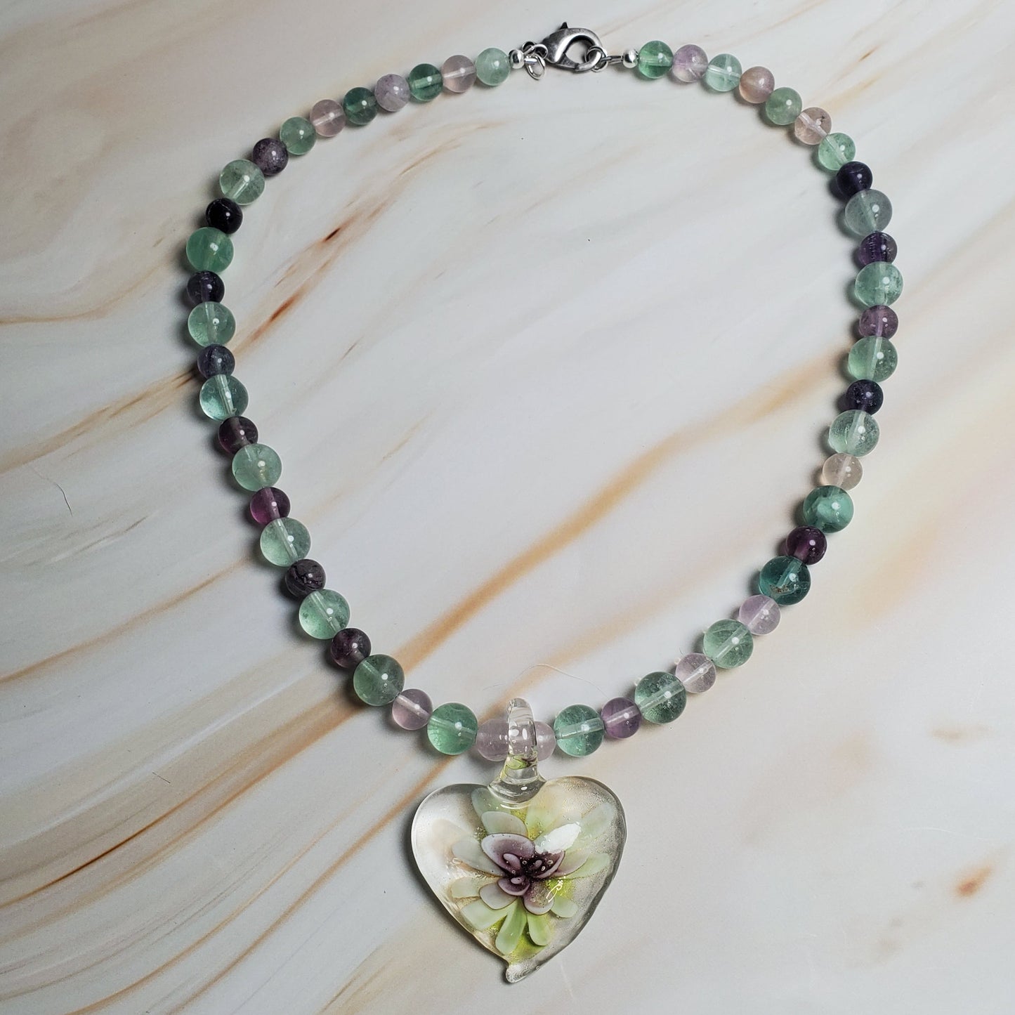 Beaded necklace with a heart-shaped pendant on a marble surface