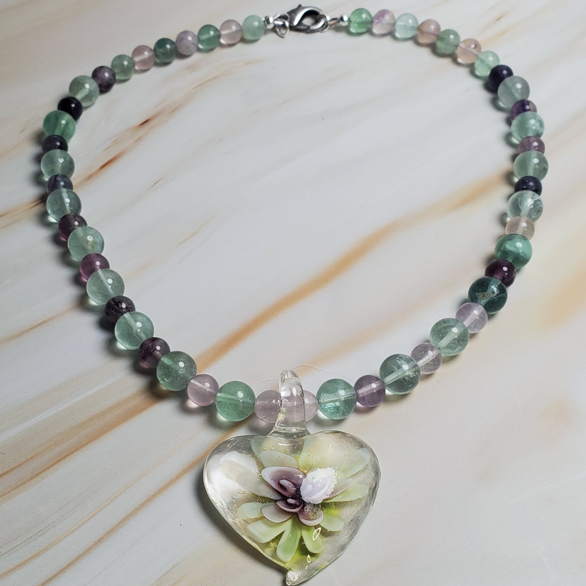 Beaded necklace with a heart-shaped charm on a marble surface