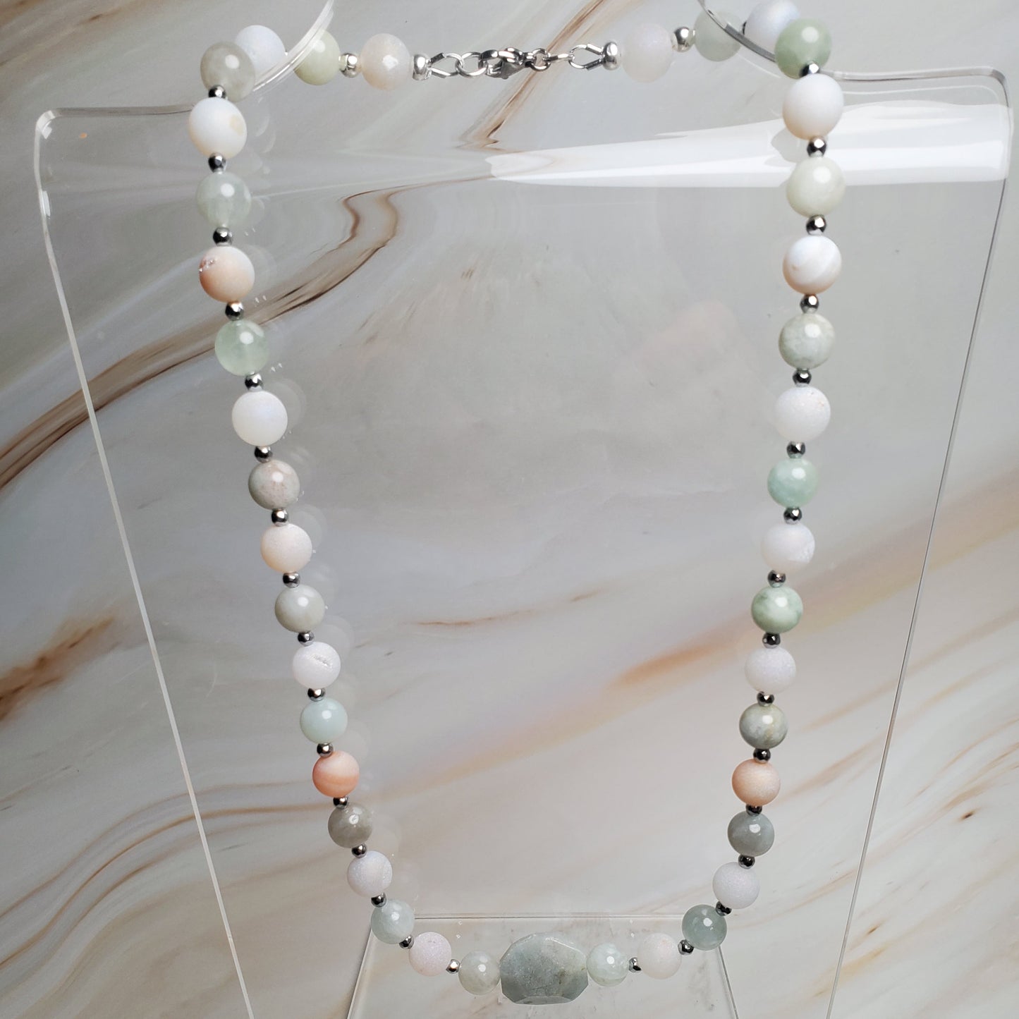 Necklace with beads on a clear stand against a marble background