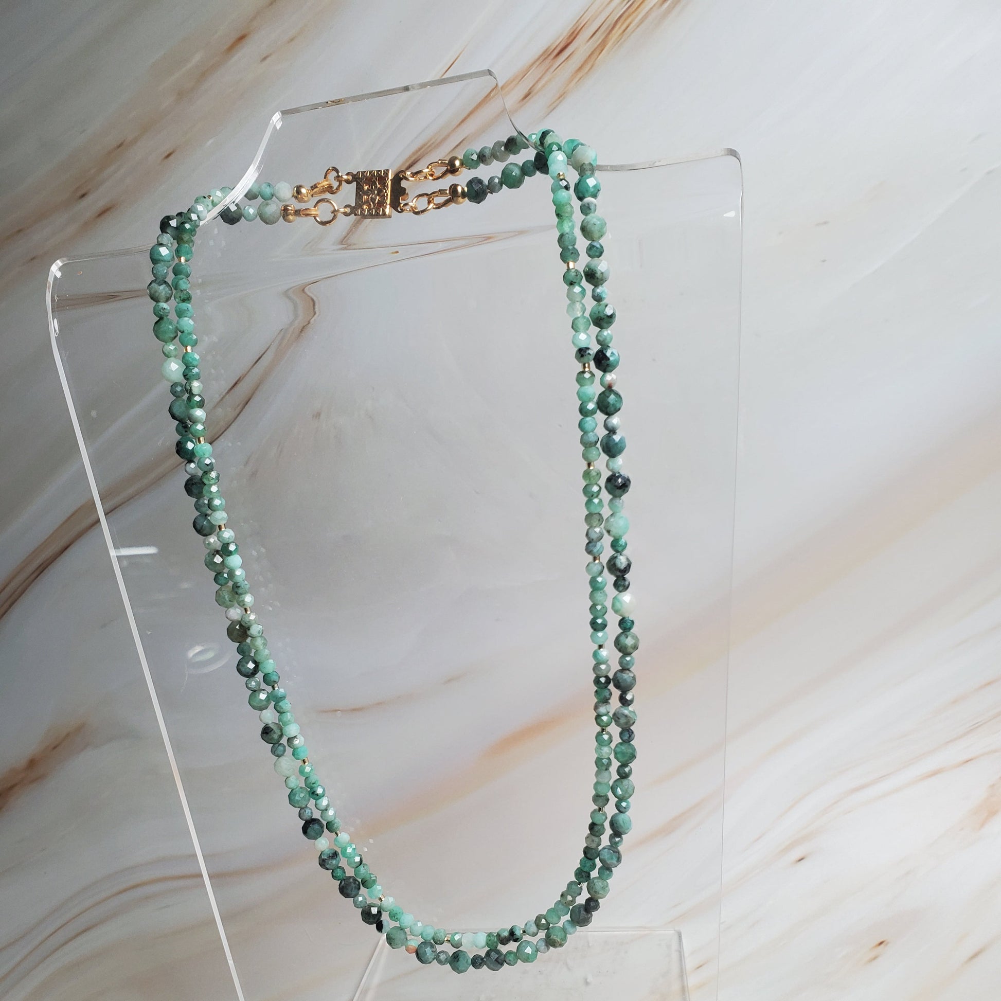 Green beaded necklace on a clear stand against a marble background