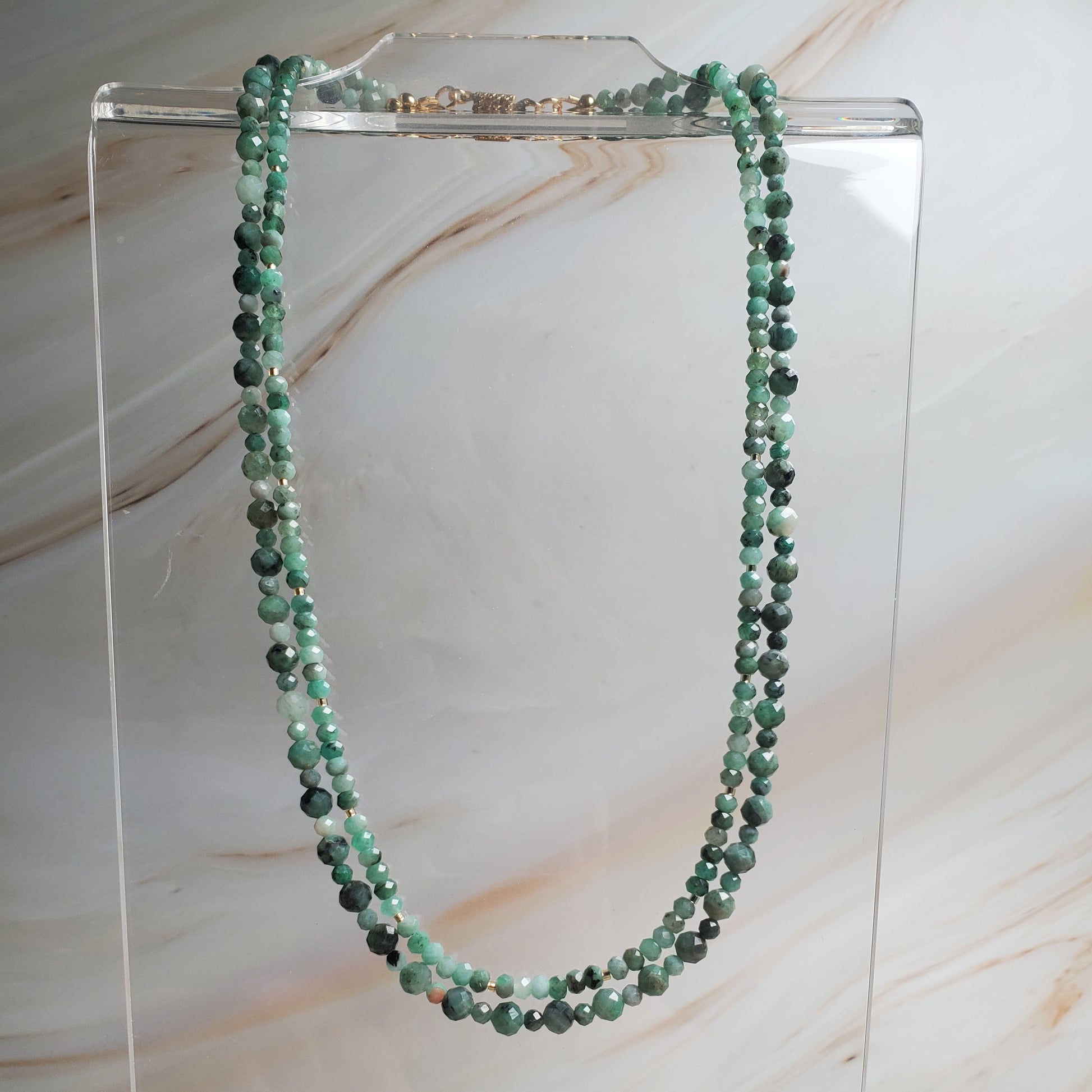 Green beaded necklace on a clear stand against a marble background