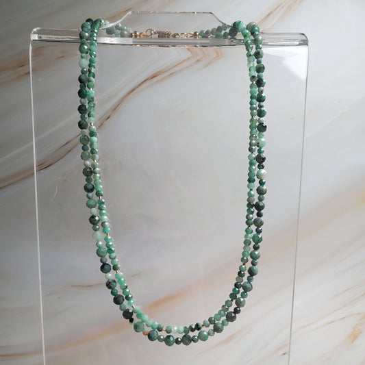 Green beaded necklace on a clear stand against a marble background
