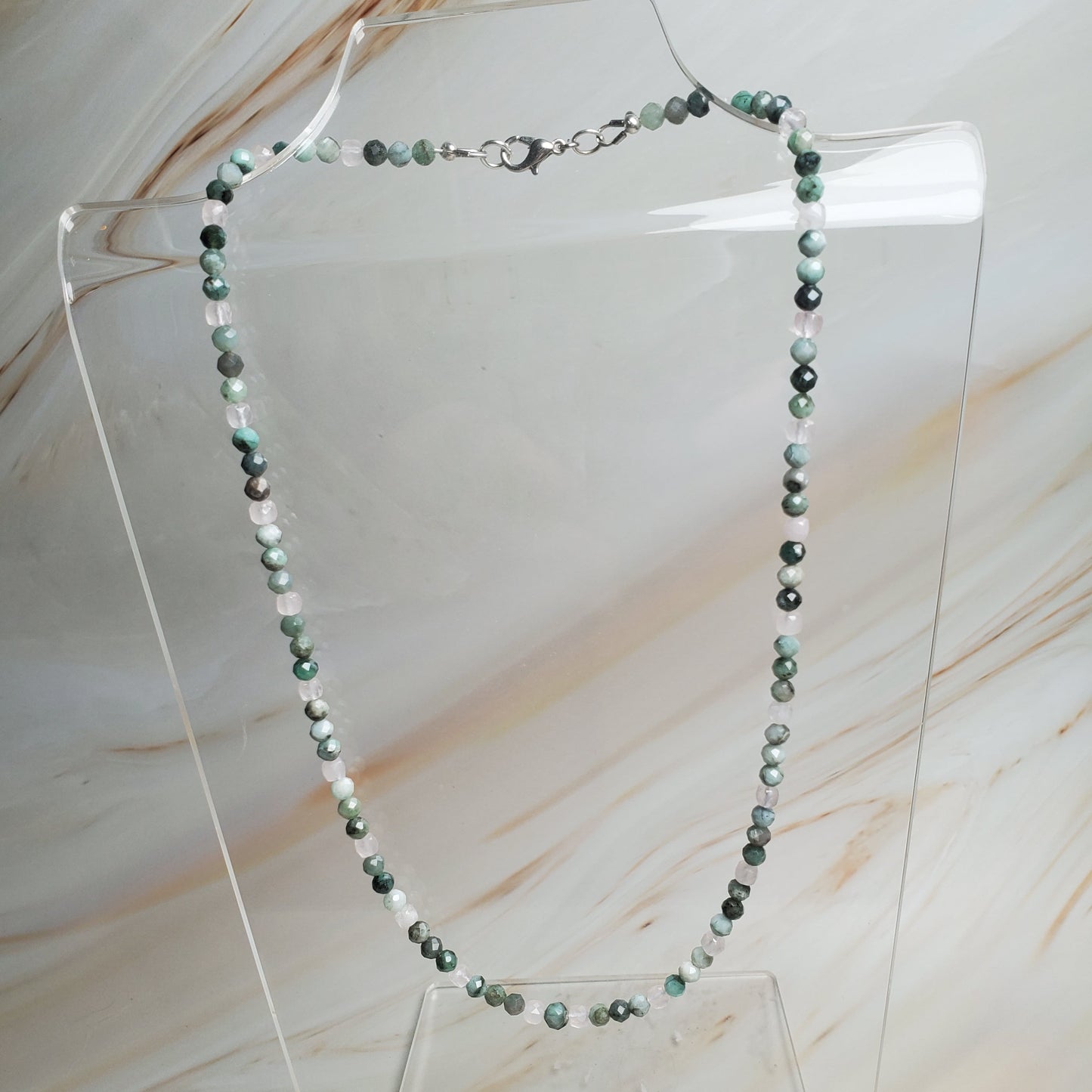 Necklace with green beads on a clear stand against a marble background