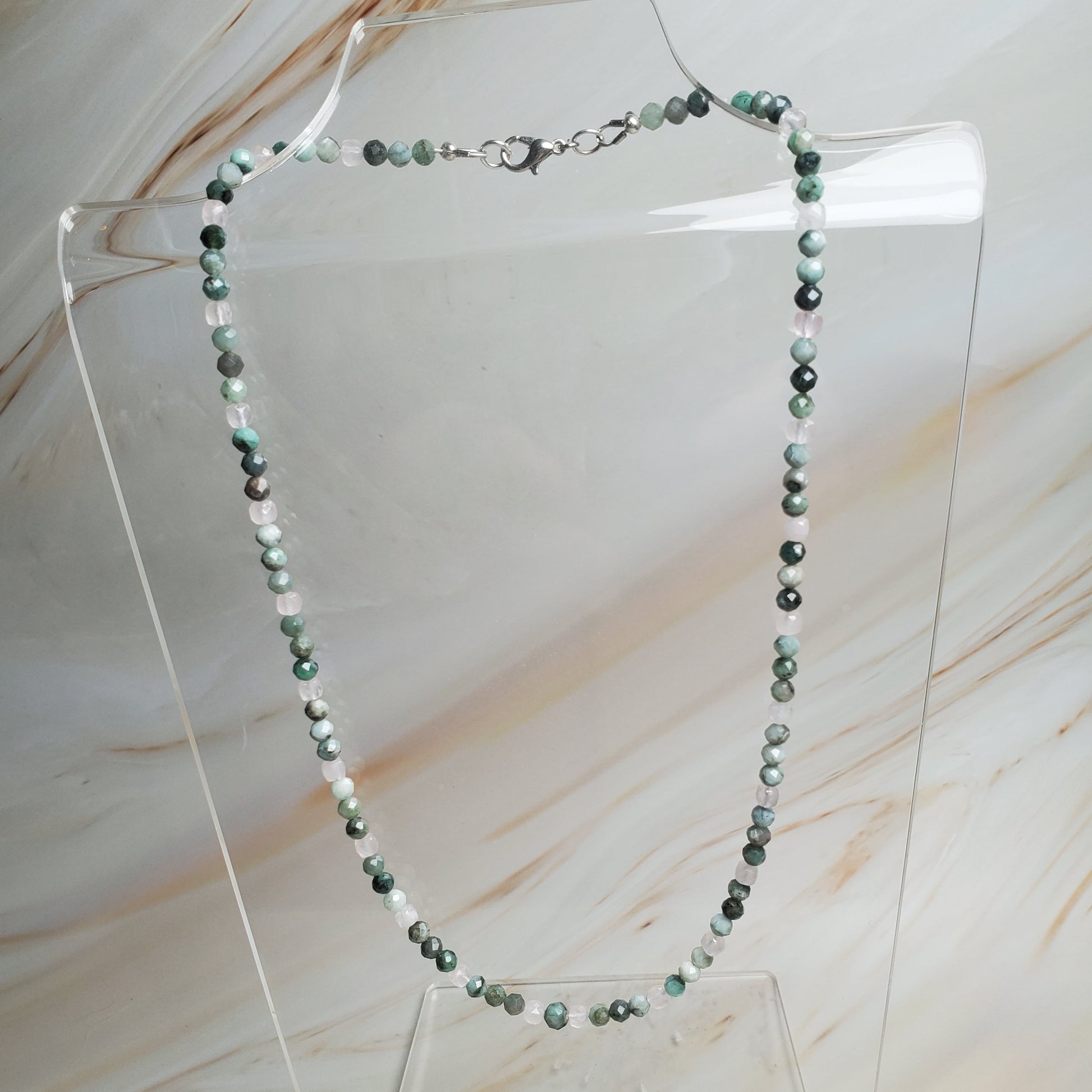 Necklace with green beads on a clear stand against a marble background