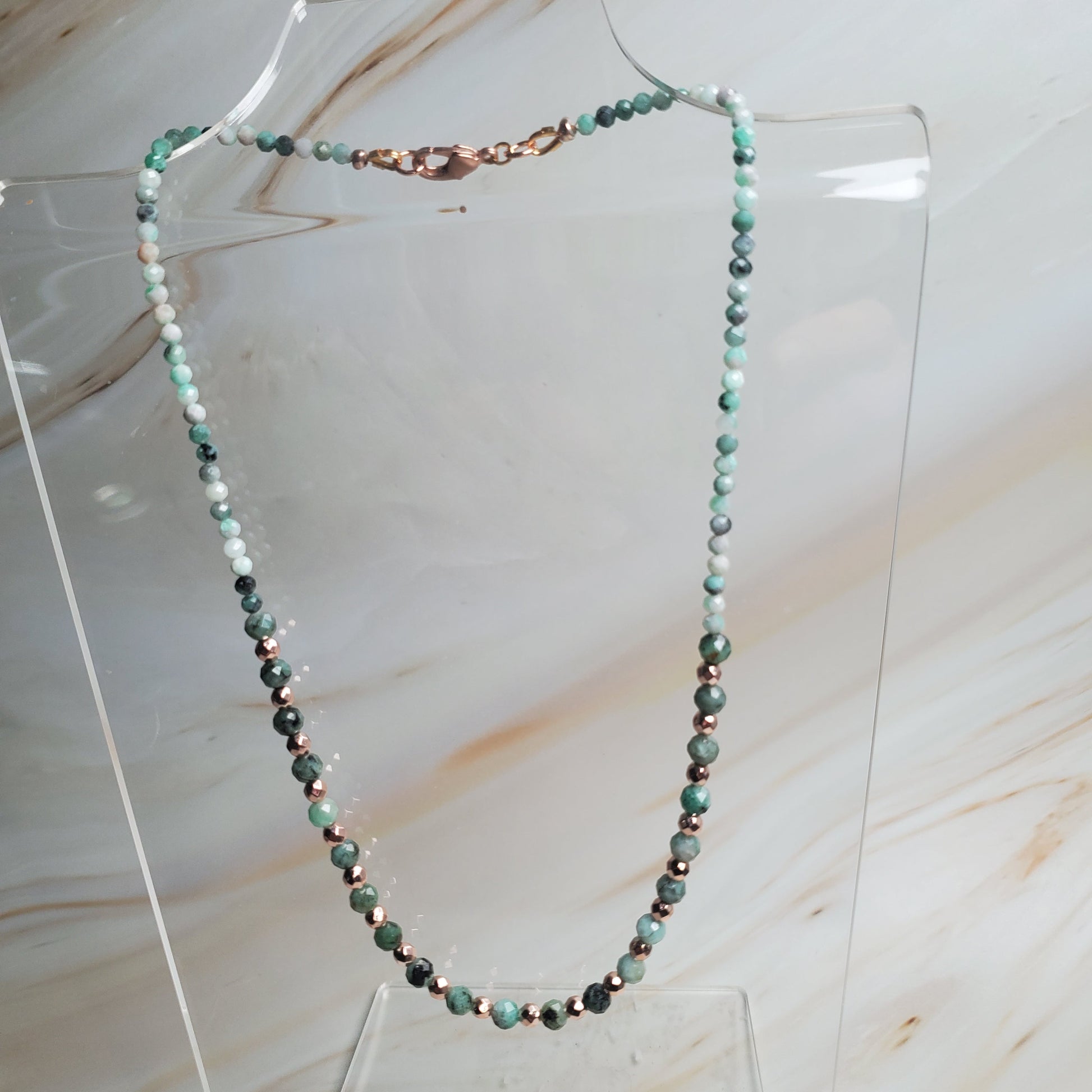 Beaded necklace on a clear stand against a marble background