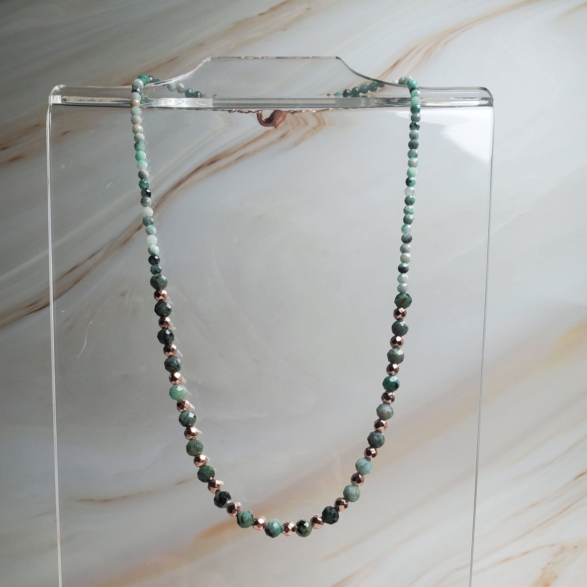 Necklace with green beads on a clear stand against a marble background