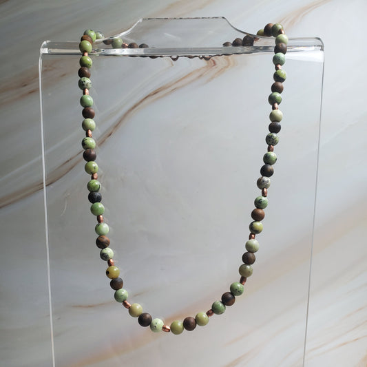 Necklace with green and brown beads on a clear stand against a marble background