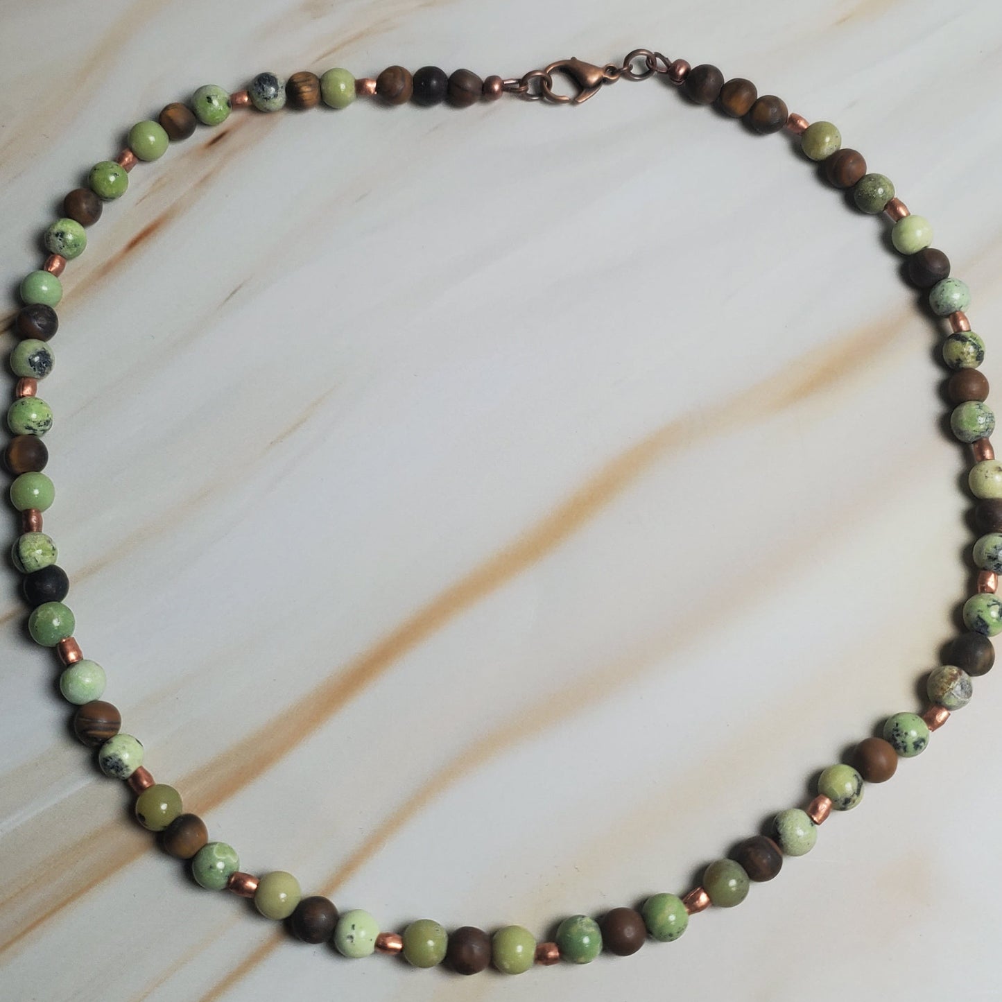 Necklace with green and brown beads on a beige fabric background